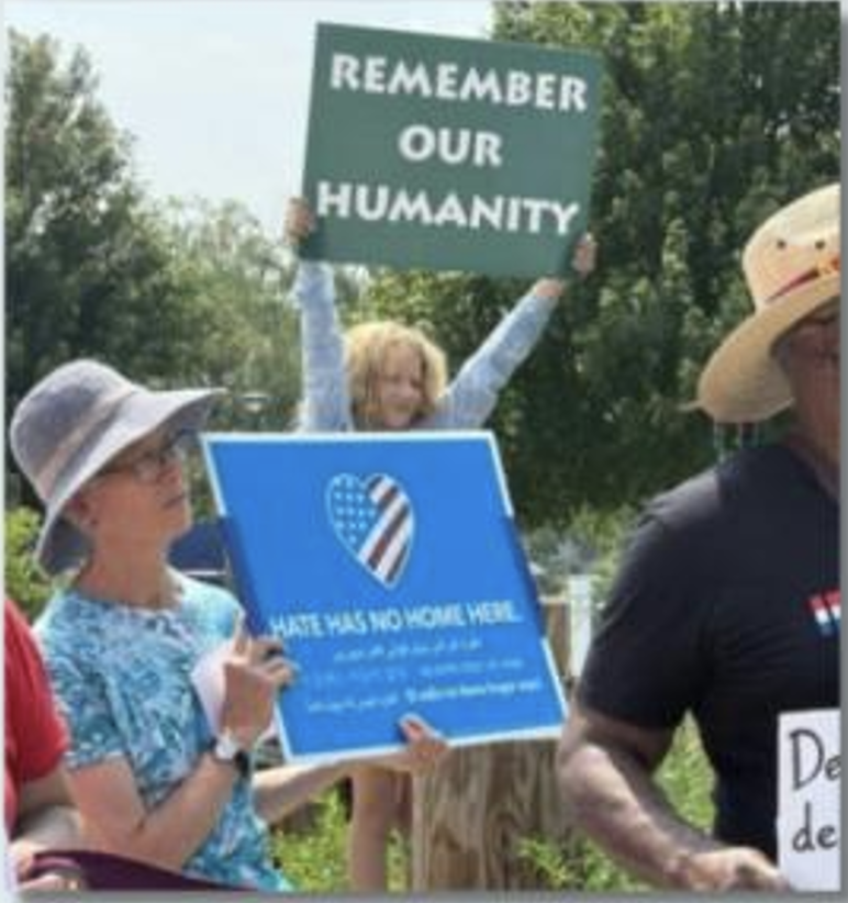 People holding up signs with "remember our humanity" and "hate has no home here"