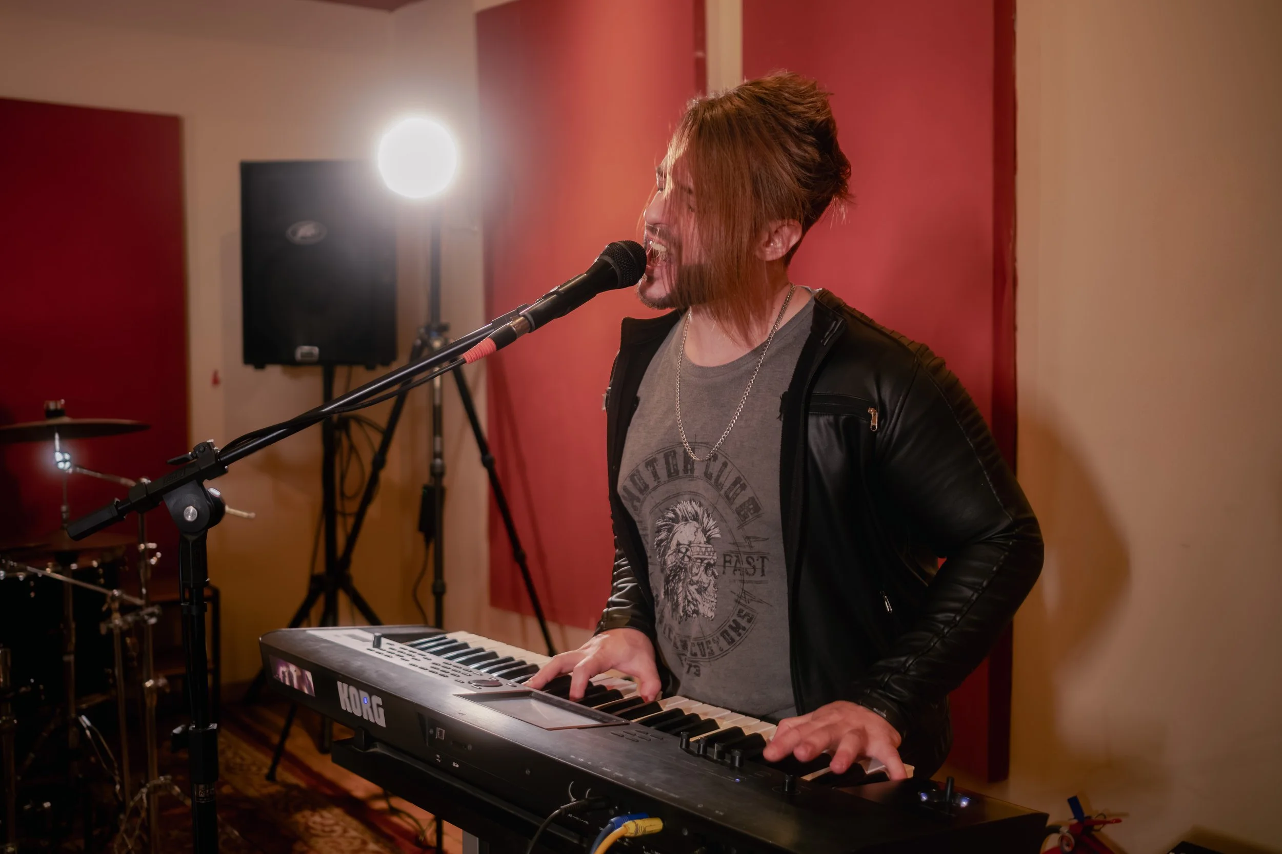 Hombre tocando piano y cantando en un escenario de grabación con micrófono