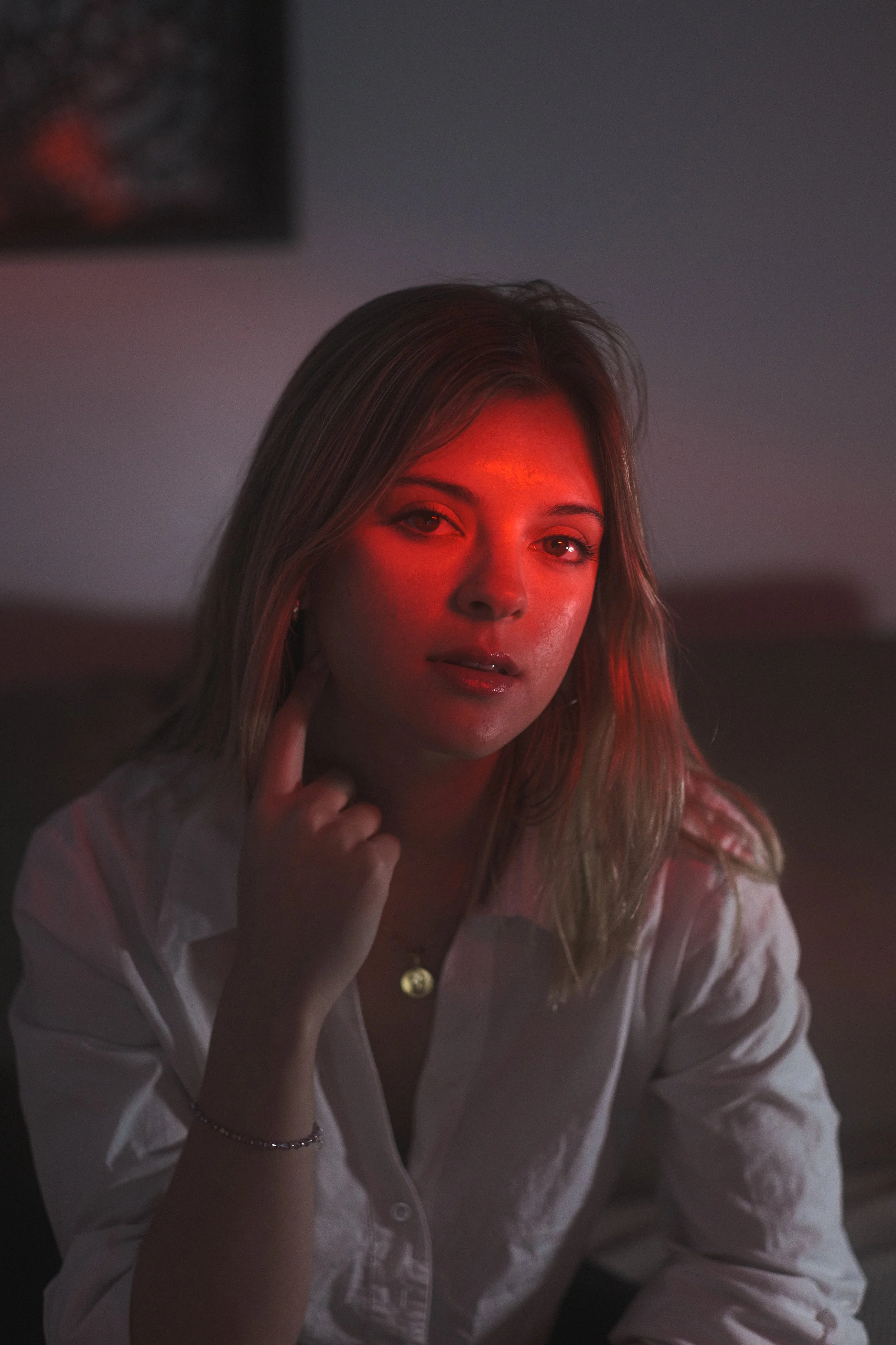 Retrato de una mujer joven con cabello rubio y ojos claros, con iluminación roja en su rostro, en un ambiente relajado y oscuro.