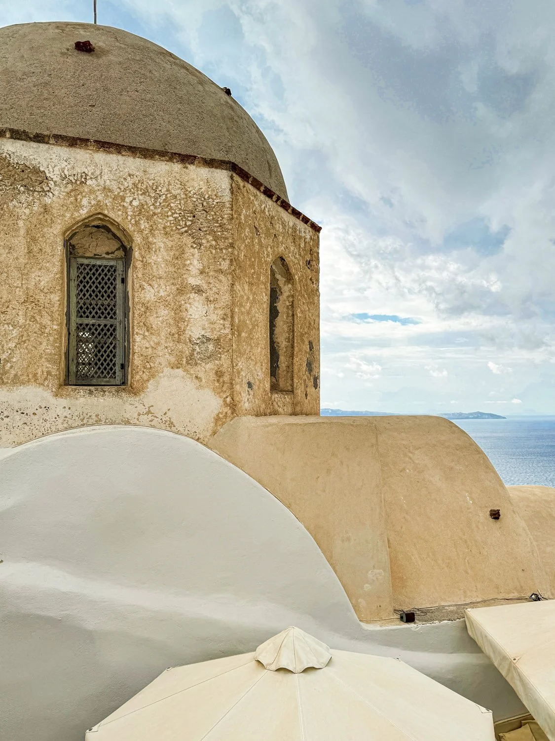  Textured beige architecture with a taupe dome in Oia, Santorini, Greece, with the sea in the background. 