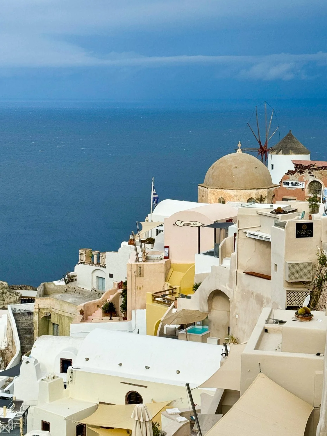  Cliffside village of Oia, Santorini, with windmill and Greek flag overlooking the Aegean Sea. 