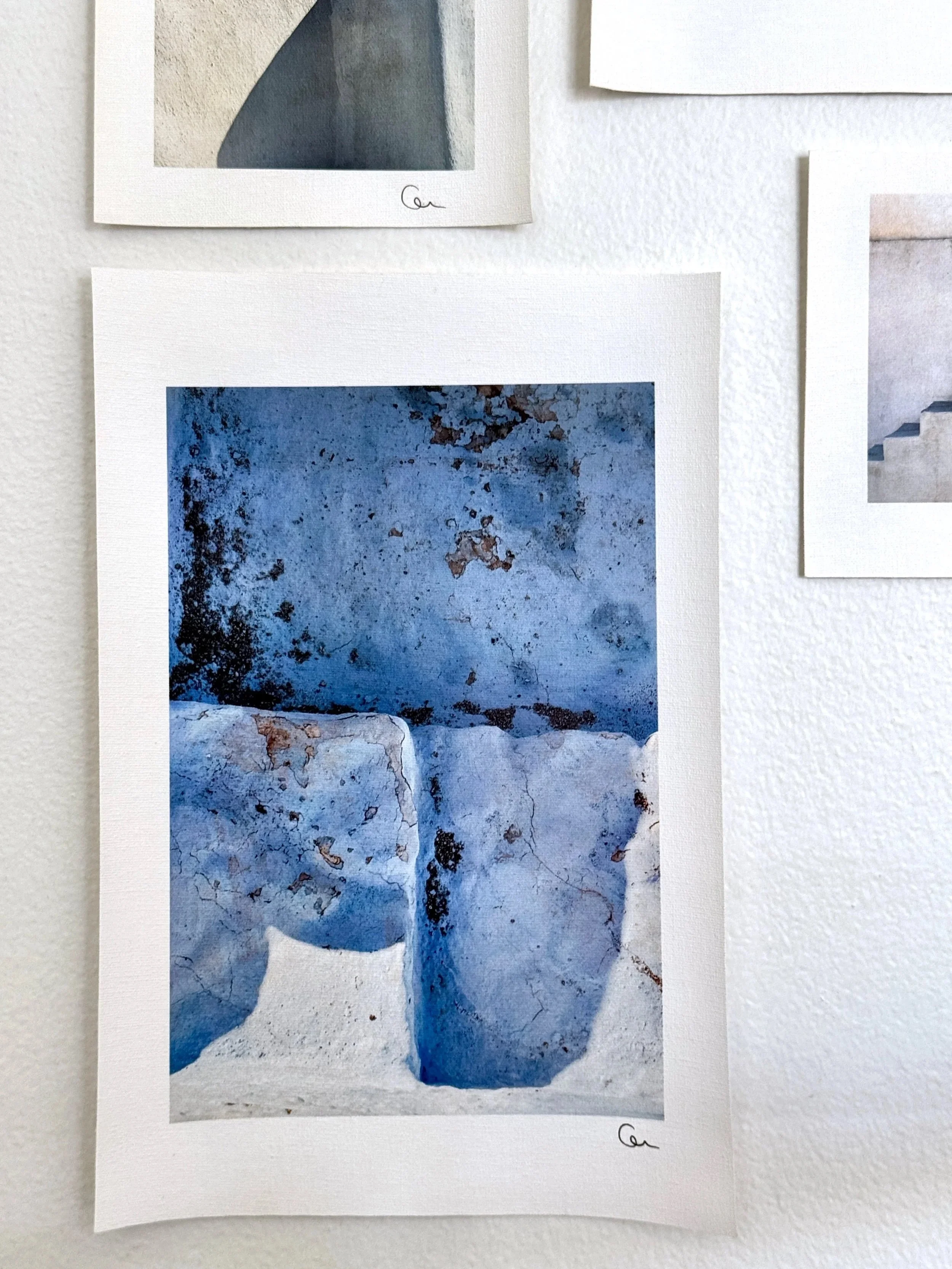 Close-up of a small photographic print from Galanopoulos Art Gallery showing weathered blue and white Cycladic architecture with cracked, textured surfaces.