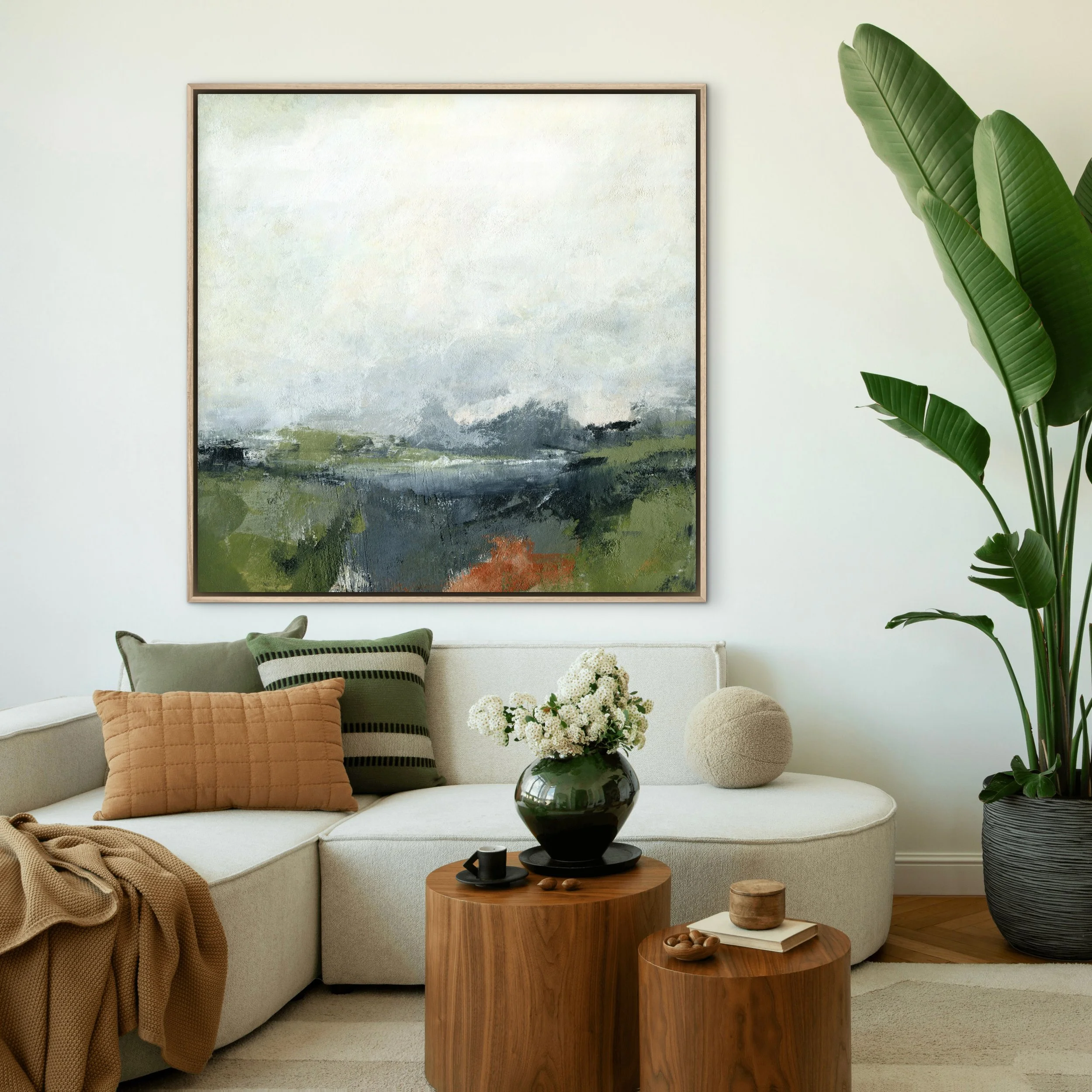 Escape abstract landscape art print by Melanie Biehle in blue-gray, olive green, and rust, displayed above a cream sofa with green and ochre pillows.