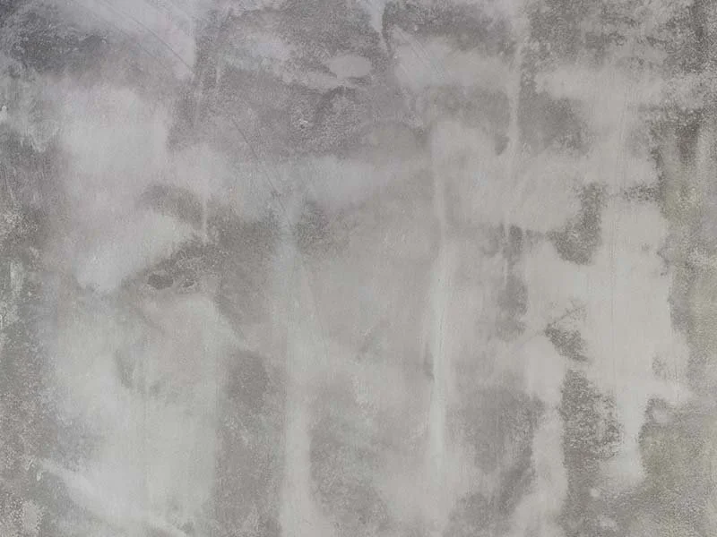Close-up of a weathered concrete or plaster wall with patches of discoloration and rough texture.