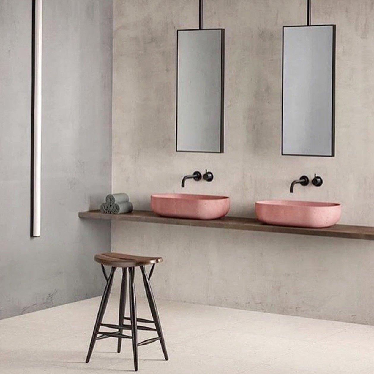 Minimalist bathroom with two pink vessel sinks, two rectangular mirrors, and a small wooden stool.