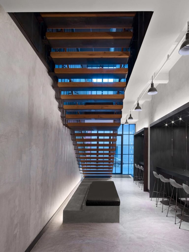 Modern interior with a floating wooden staircase turned upside down, a bench underneath, and bar seating along the wall.