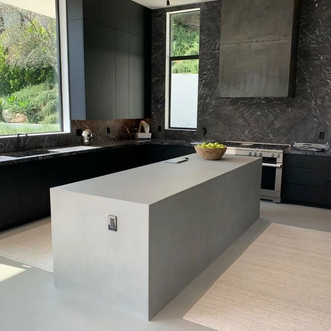 Modern kitchen with black cabinets, marble countertops, gray walls, a large white kitchen island, and green apples in a bowl.