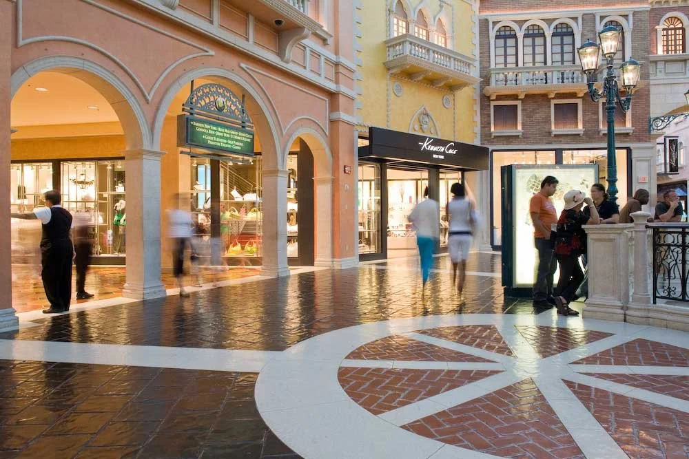 Indoor shopping mall with European-style architecture, people walking, and storefronts with glass displays.