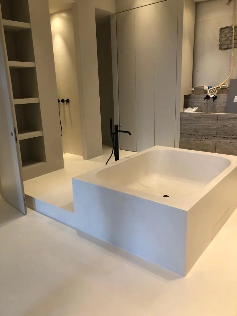 A modern bathroom with a built-in bathtub, gray cabinets, open shelves, and a partially finished wall with exposed wiring.
