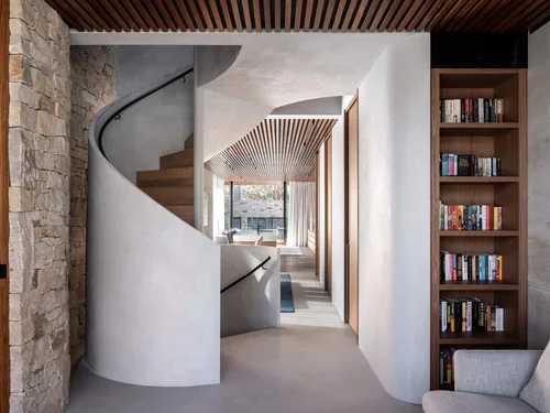 Modern interior with a curved staircase, a bookshelf filled with books, and a wooden ceiling detail.