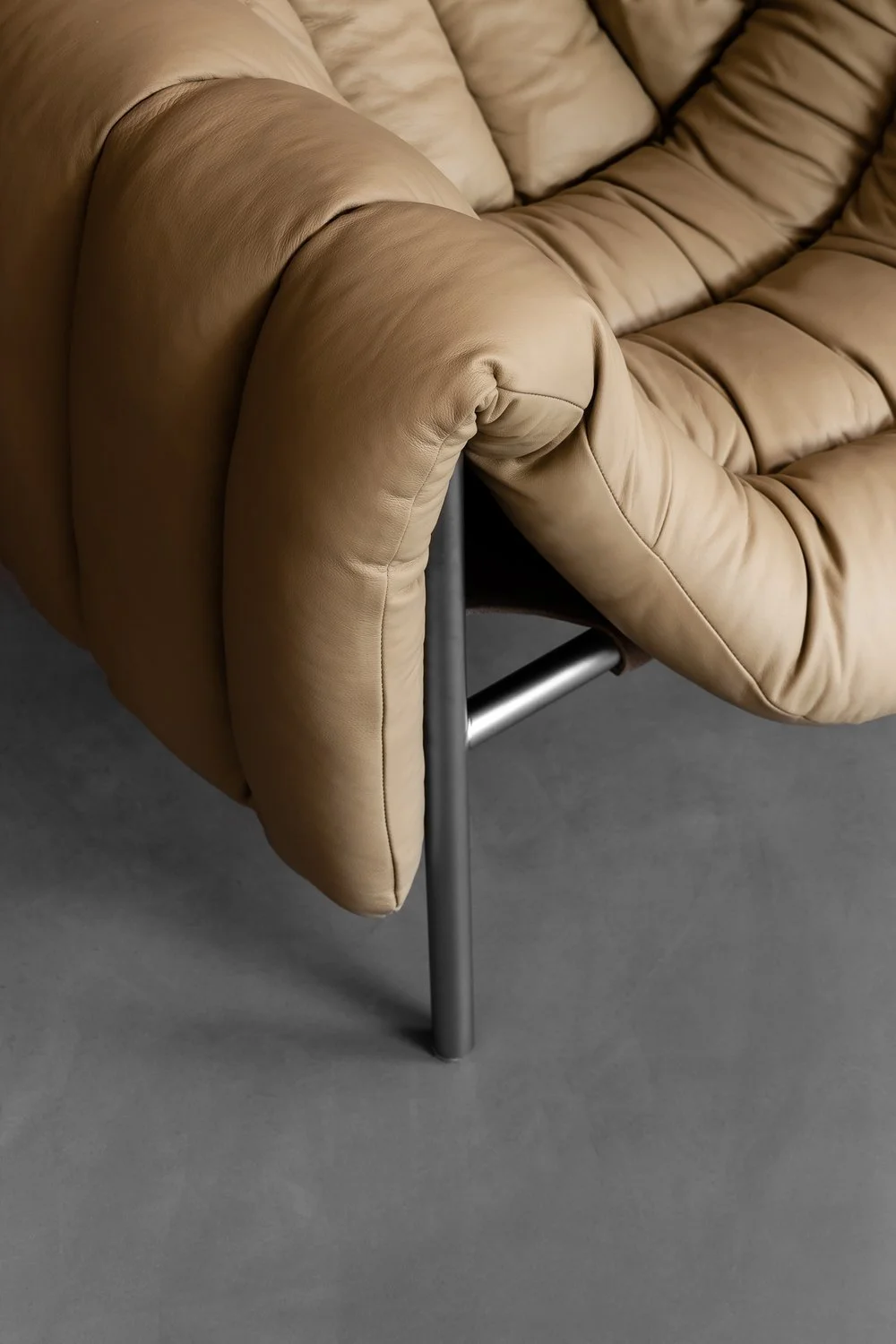 Close-up of a tan leather sofa with a modern metal leg on a gray floor.