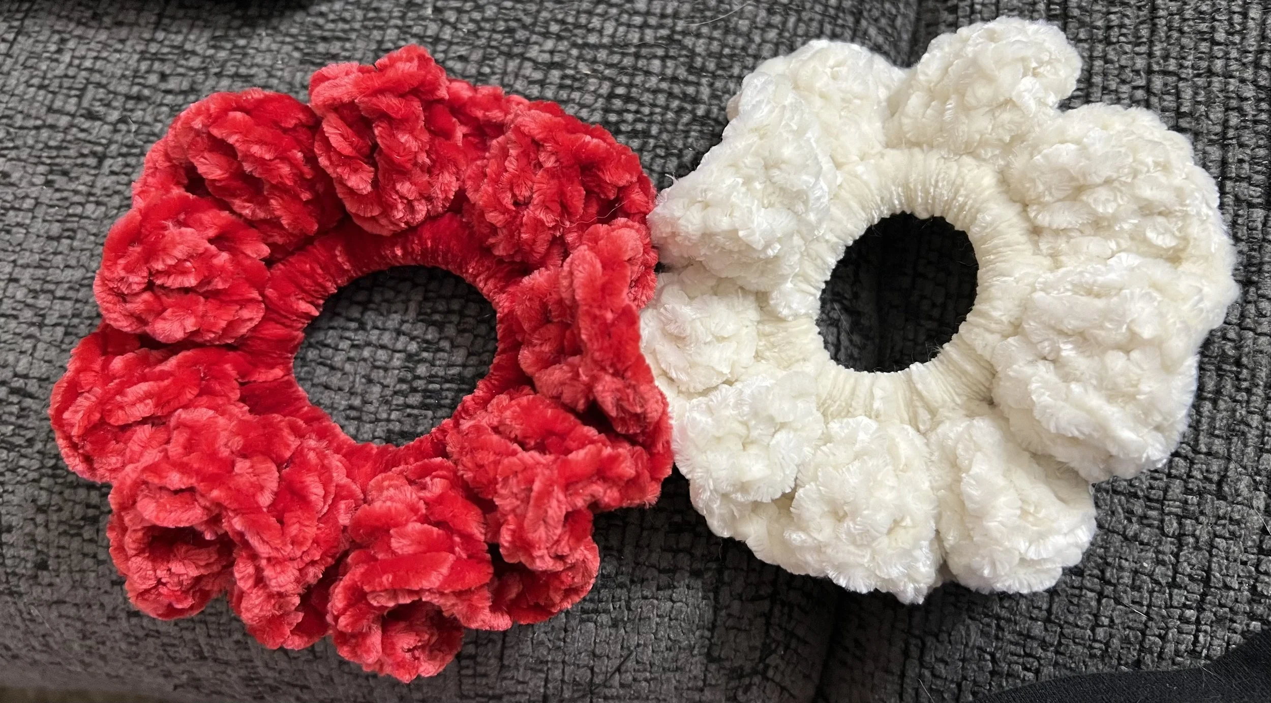 Three fluffy scrunchies, one red and two white, placed on a textured black surface.