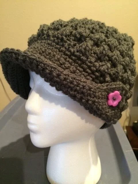 A mannequin head wearing a thick, dark brown crocheted winter hat with a pink flower embellishment.