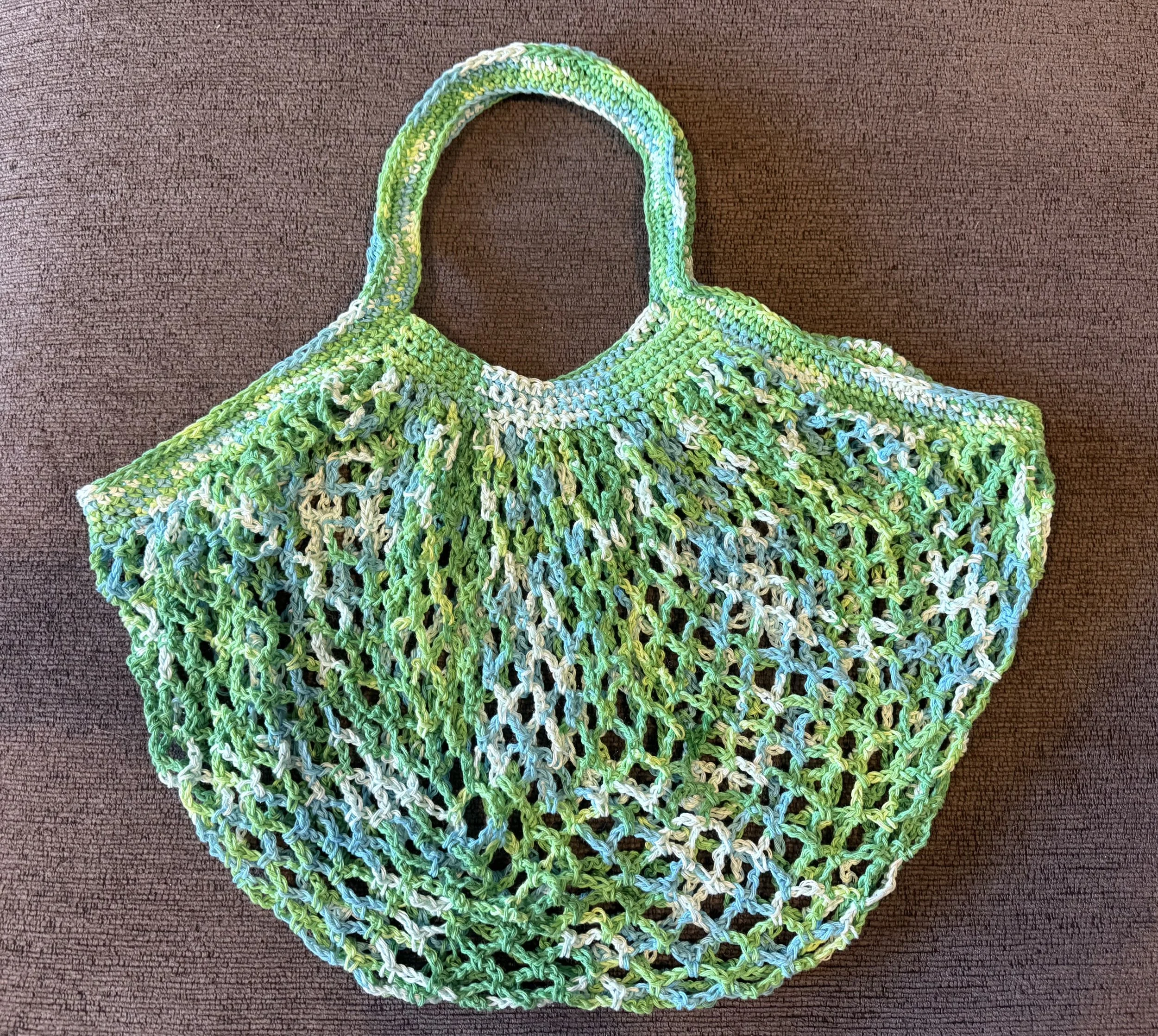 Colorful crocheted bag with shades of green, white, and blue, on a brown textured surface.
