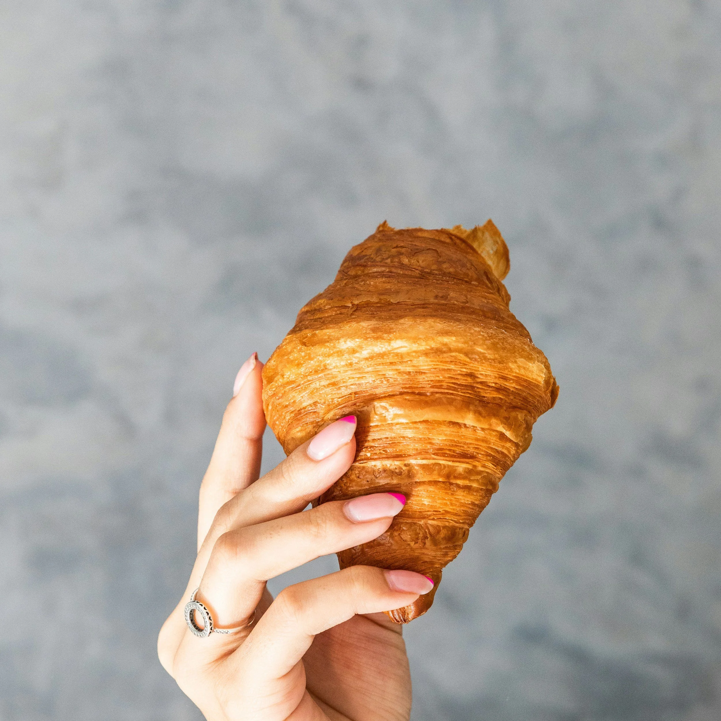 A person holding a croissant with a cloudy sky in the background.