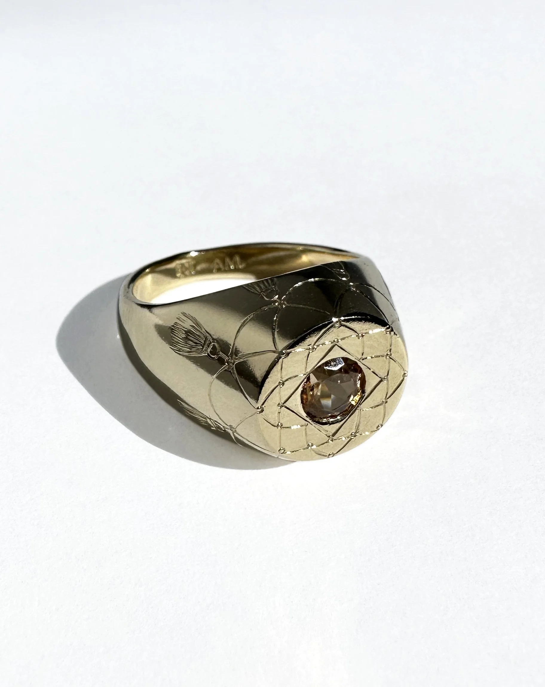 Gold ring with a central gemstone and engraved designs on the surface.