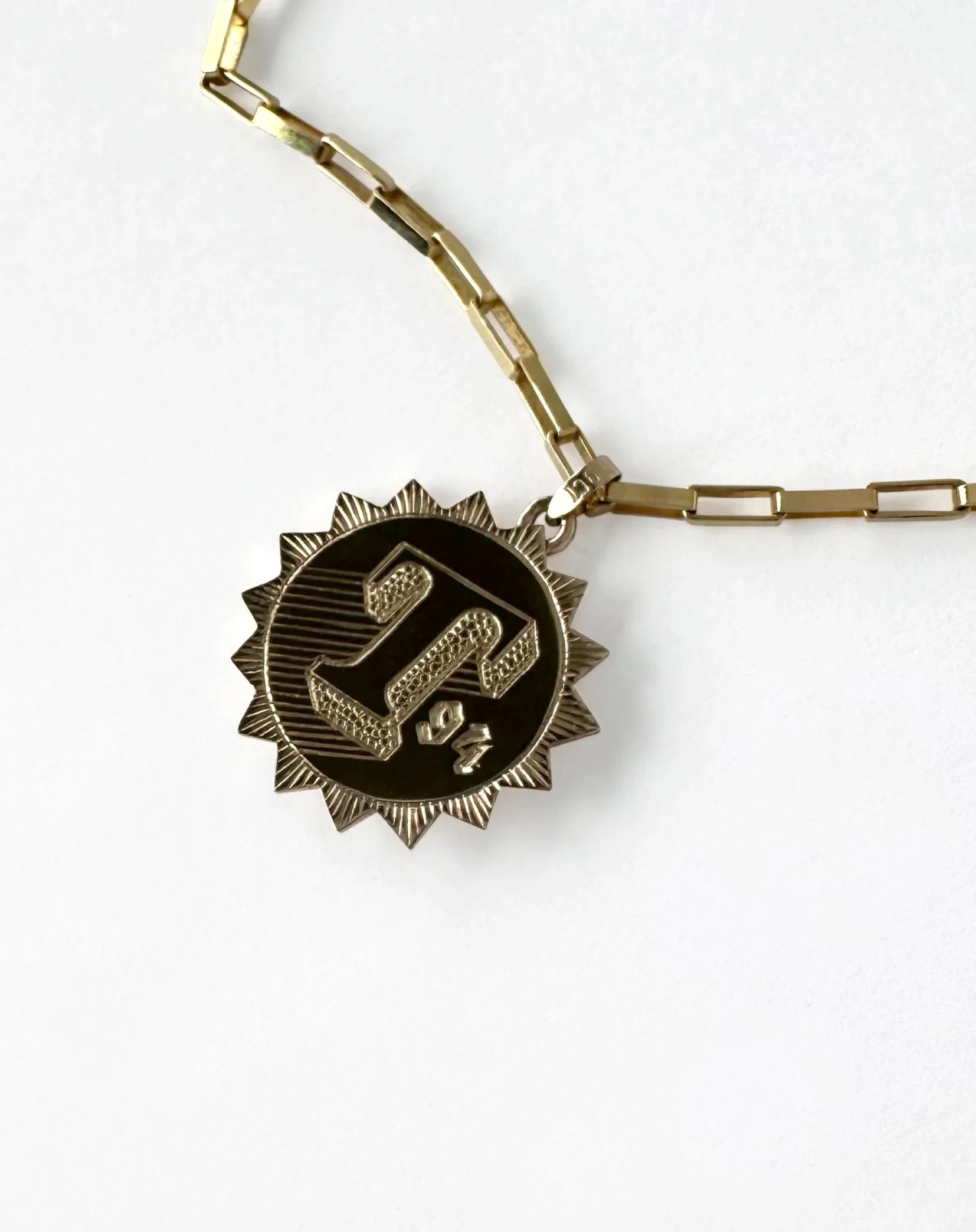 A silver chain necklace with a medal pendant featuring the number 1/4 and a sunburst design.