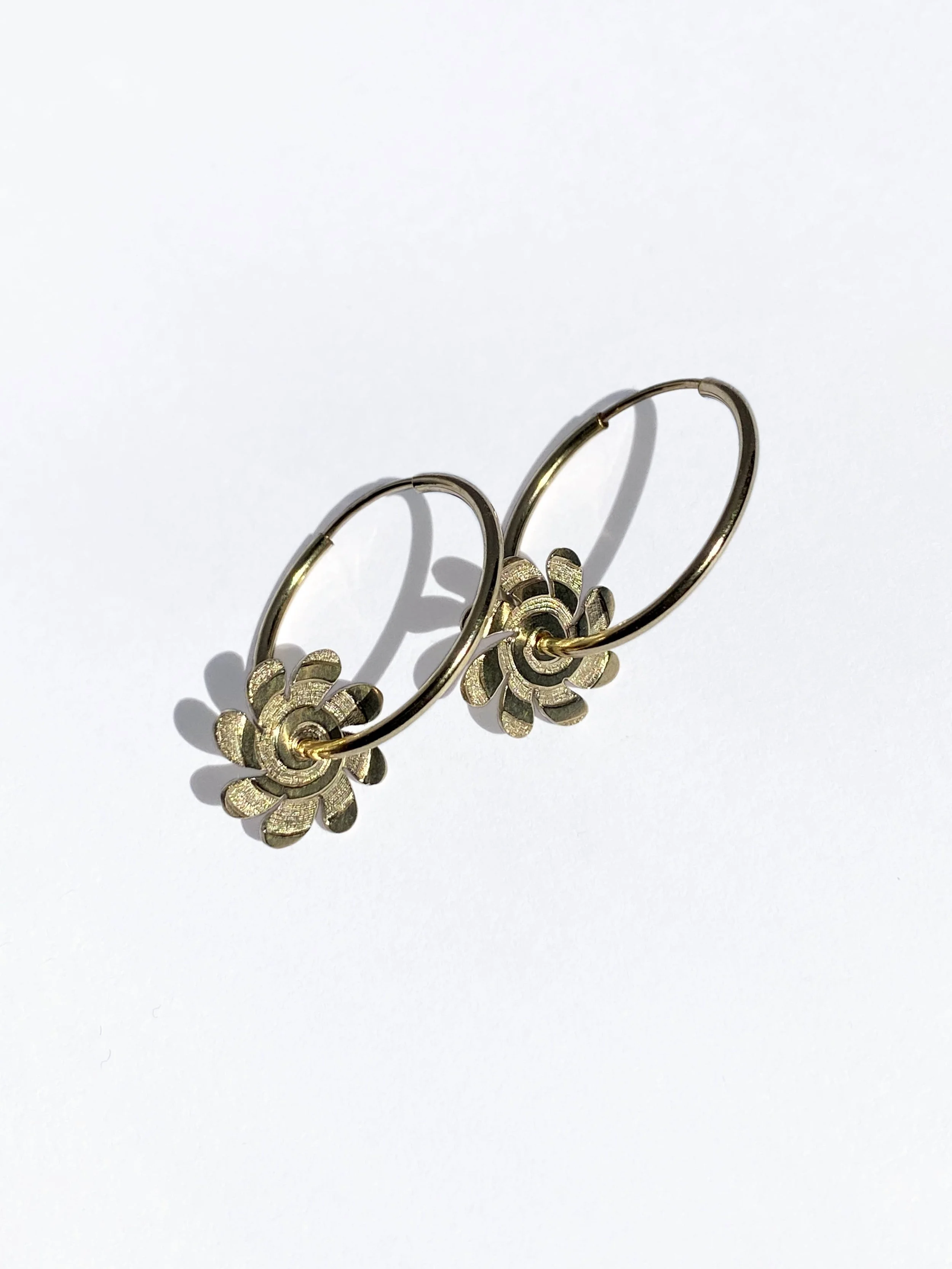 Engraved gold hoop earrings with flower-shaped charms.