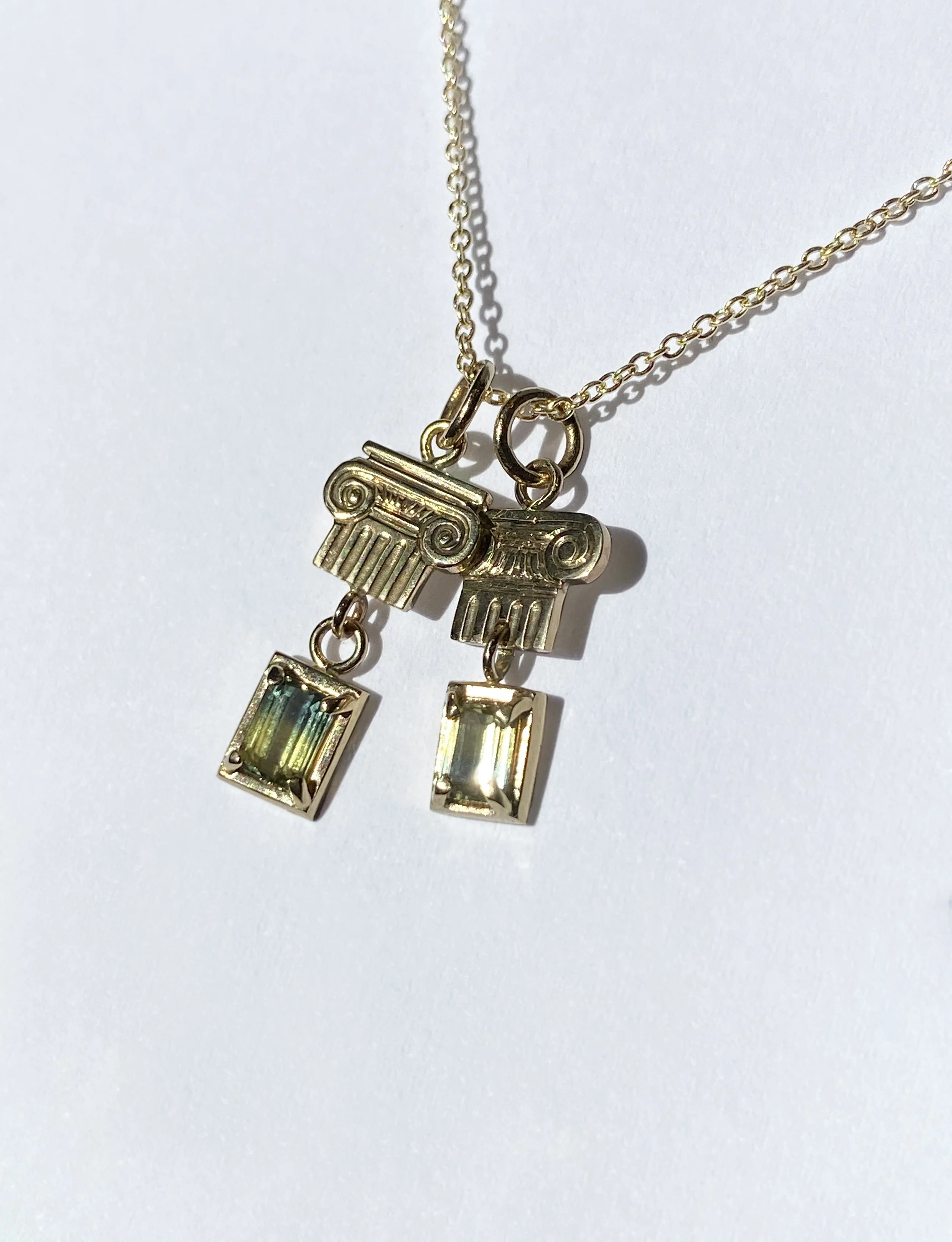 Gold necklace with two charms resembling Greek columns and two rectangular gemstone pendants.