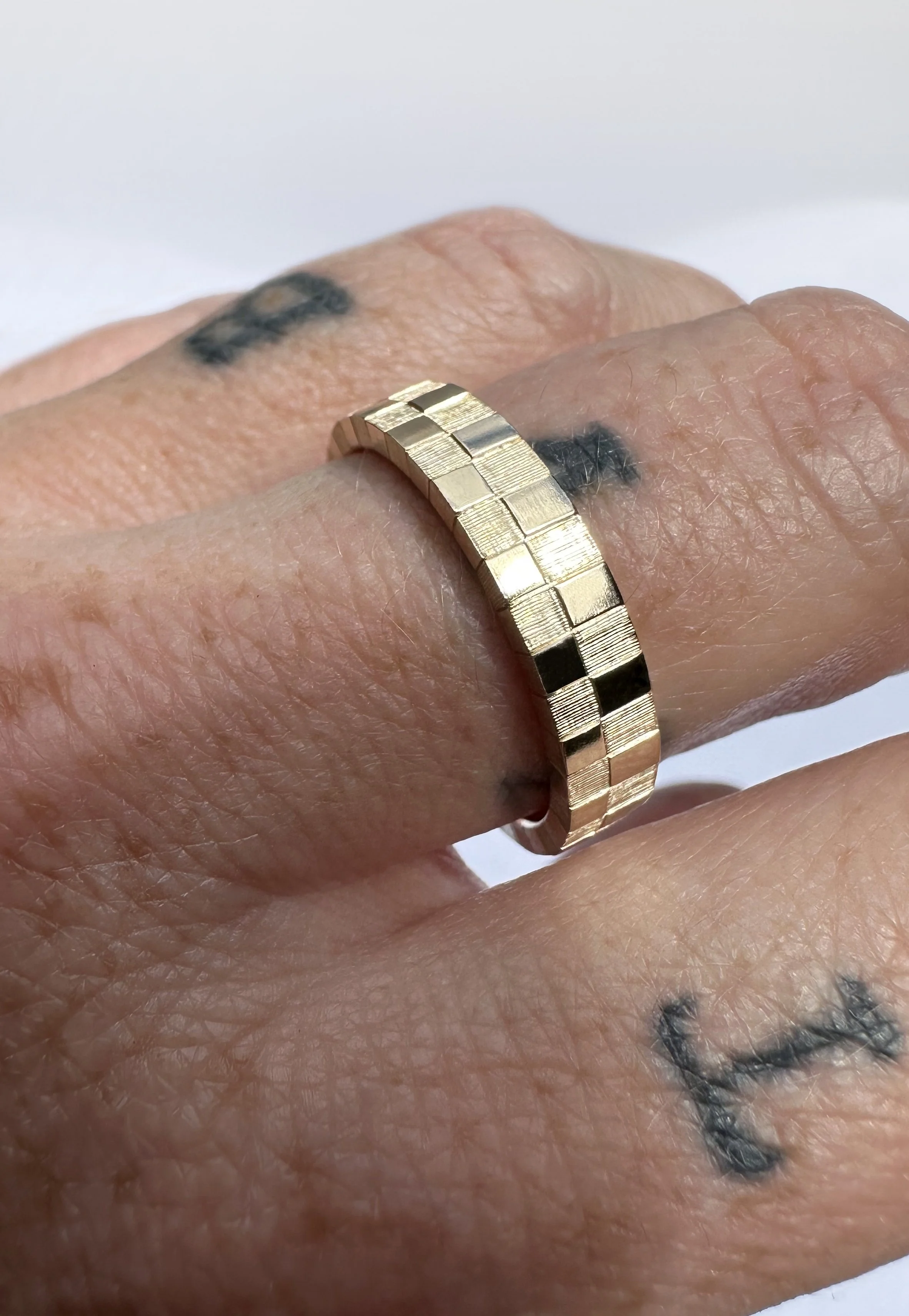 A yellow gold ring with a hand engraved check pattern.