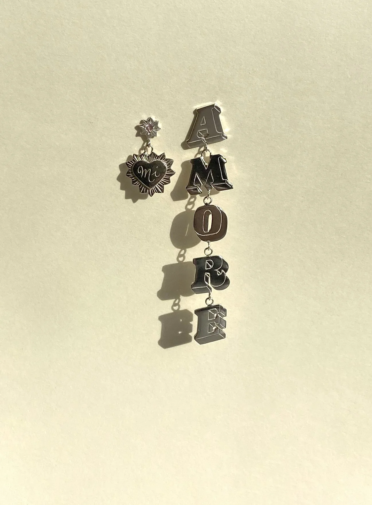 Amore earrings. The left earring has a 'Mi' engraved in a heart. The right earring spells 'Amore'. Each letter is hand engraved and connected with a link. 