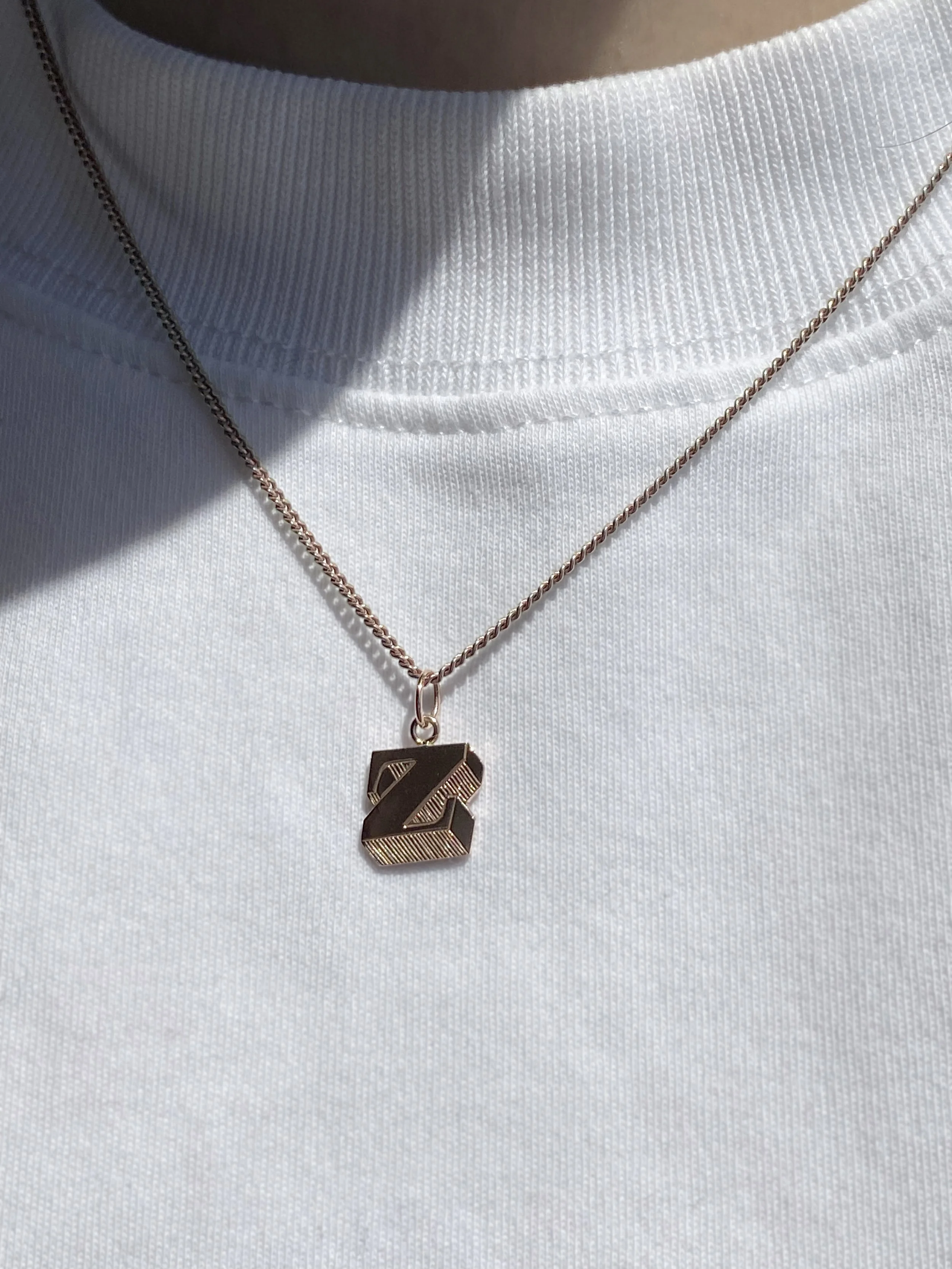 A close-up of a person's neck wearing a white t-shirt and a necklace with a pendant shaped like a 'Z' with gold and black coloring.