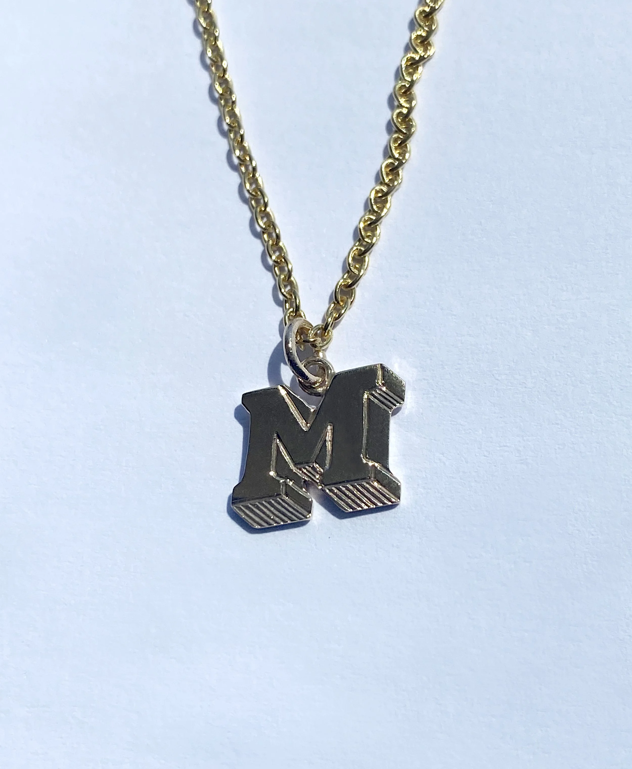 Gold chain with a pendant in the shape of the letter M.