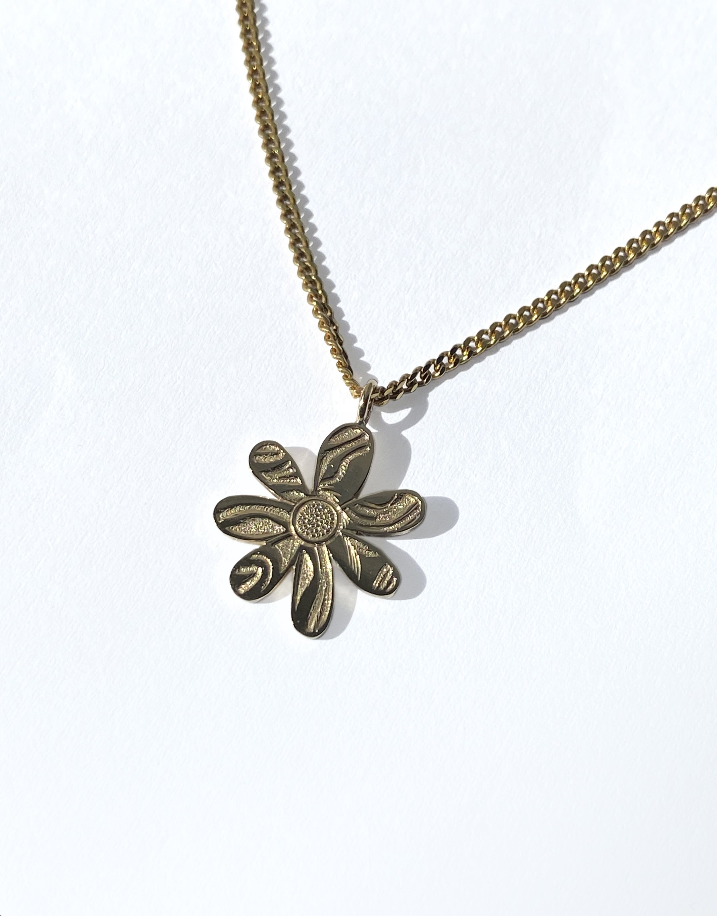 Gold chain necklace with flower-shaped pendant on a white background