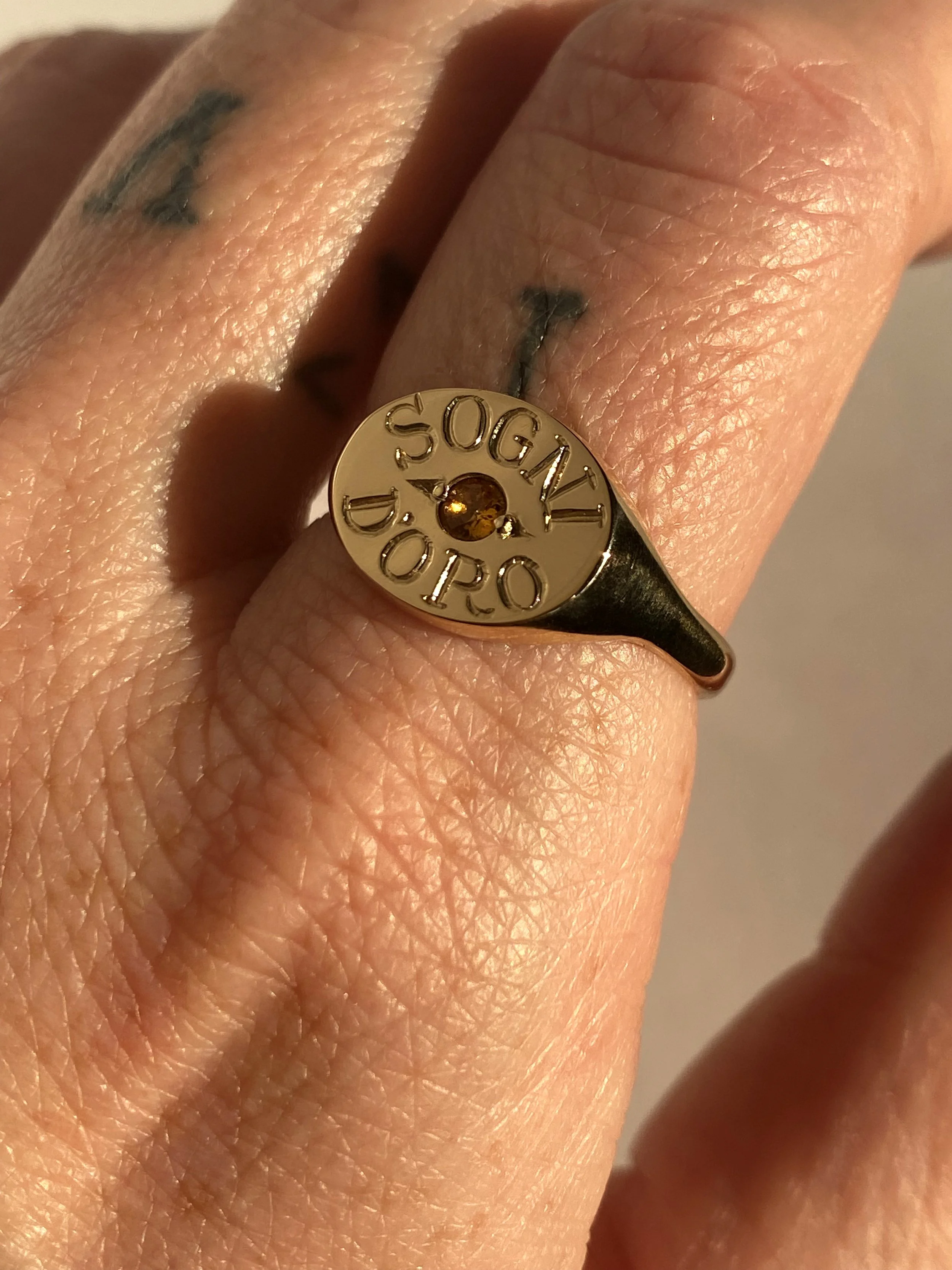 An engraved gold ring featuring a small amber-colored gemstone in the center.