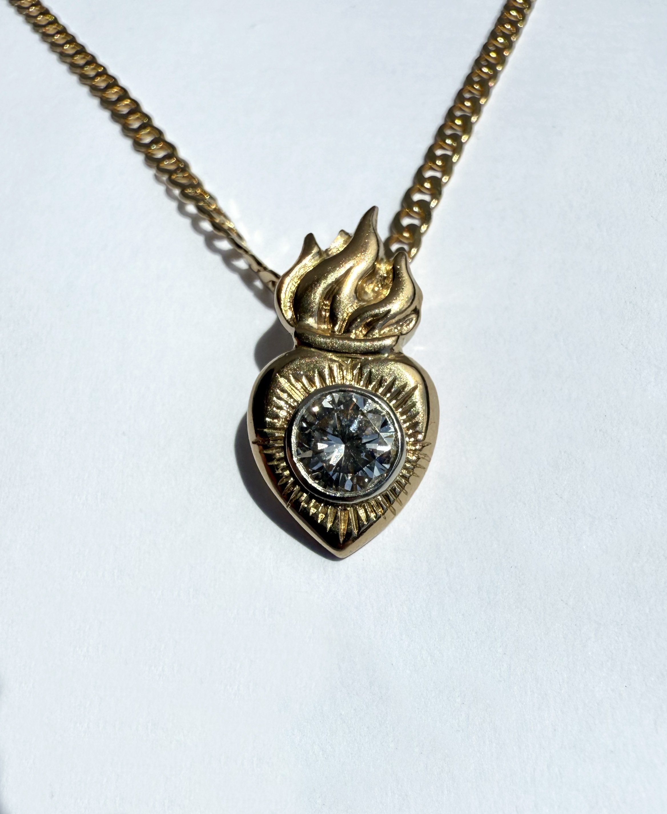 Gold necklace with a heart-shaped pendant featuring a diamond in the center and a flame design on top.