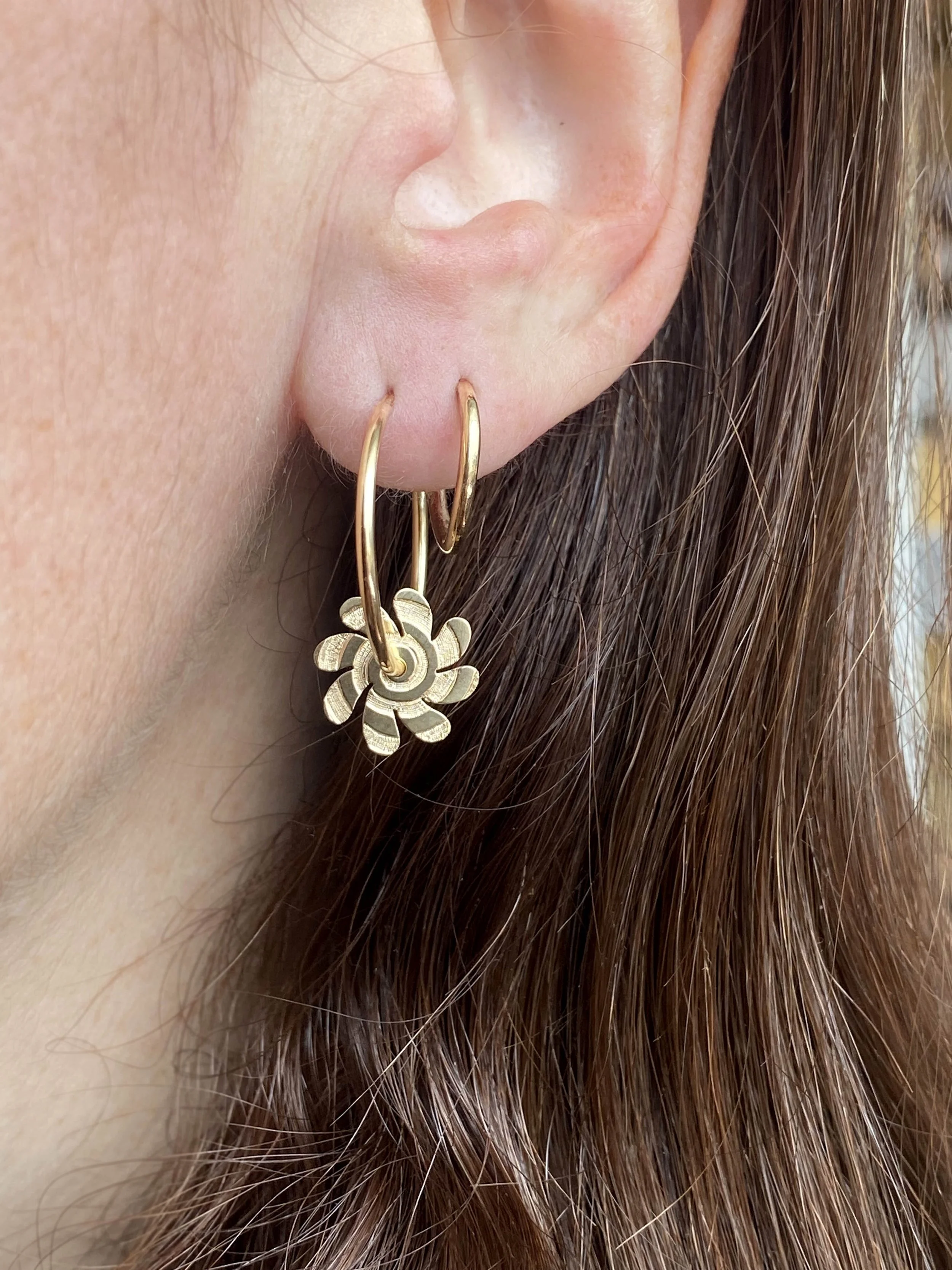 Close-up of a woman's ear wearing gold hoop earrings with a flower-shaped charm.