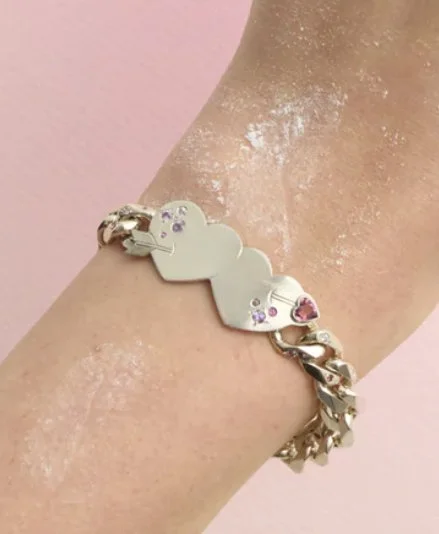 A person's ankle wearing a silver bracelet with cloud-shaped charms against a pink background.
