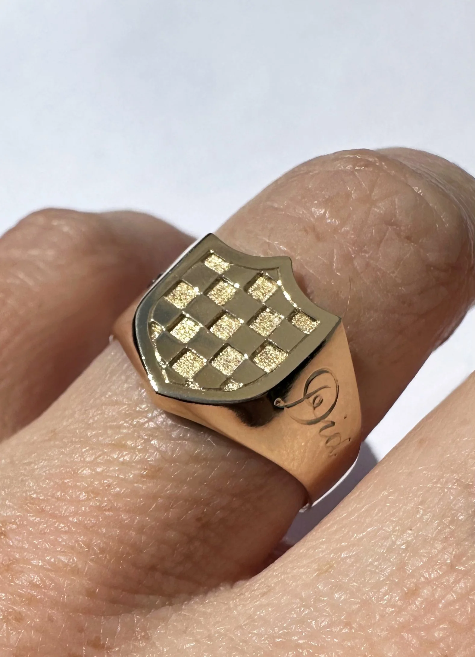 A 14k gold signet ring with a shield shape and a checkered pattern. Each square painstakingly carved and hammered to give it that sparkly effect.