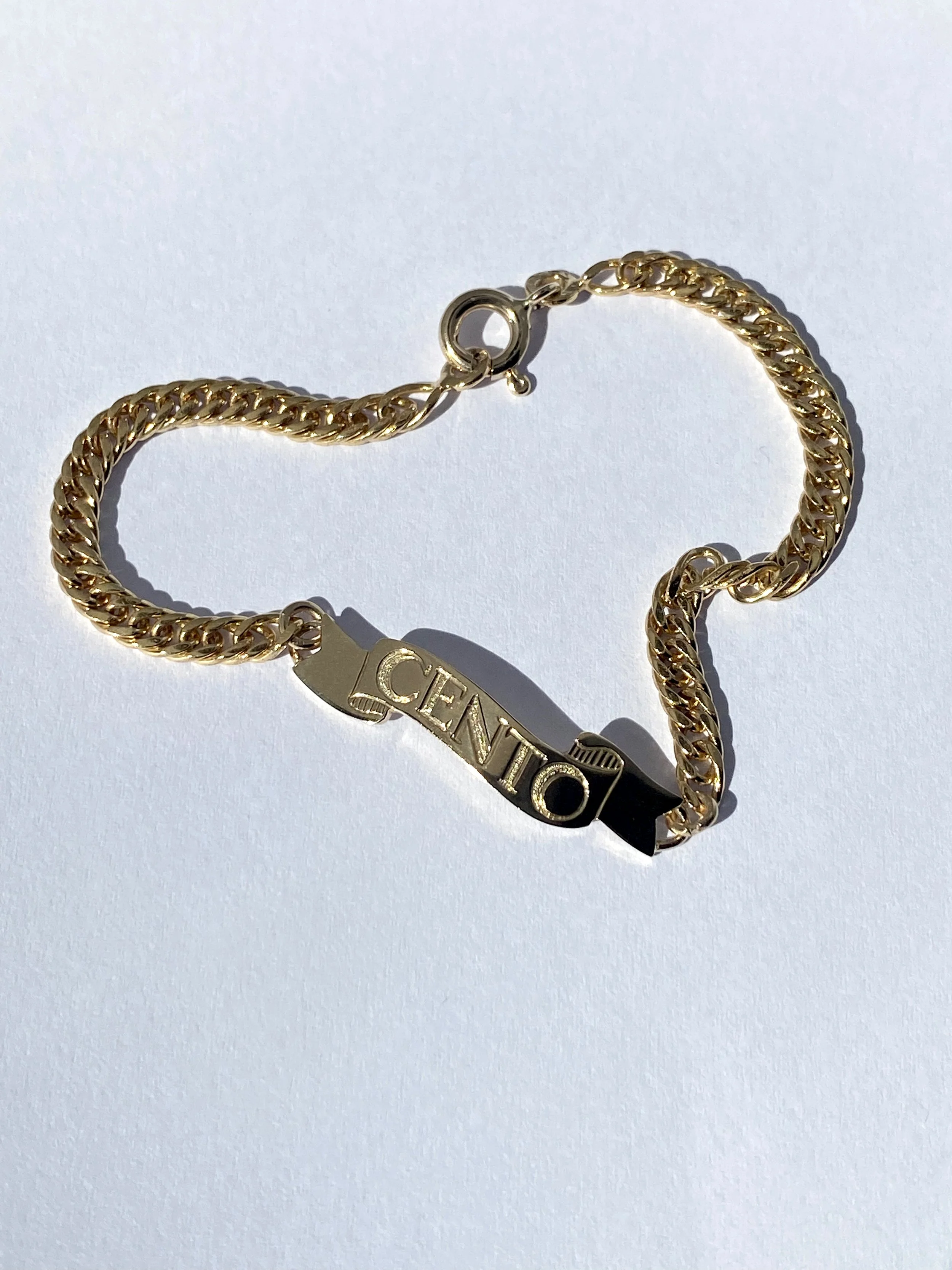 Gold bracelet with a rectangular charm inscribed with the word 'CENTIC' on a white background.