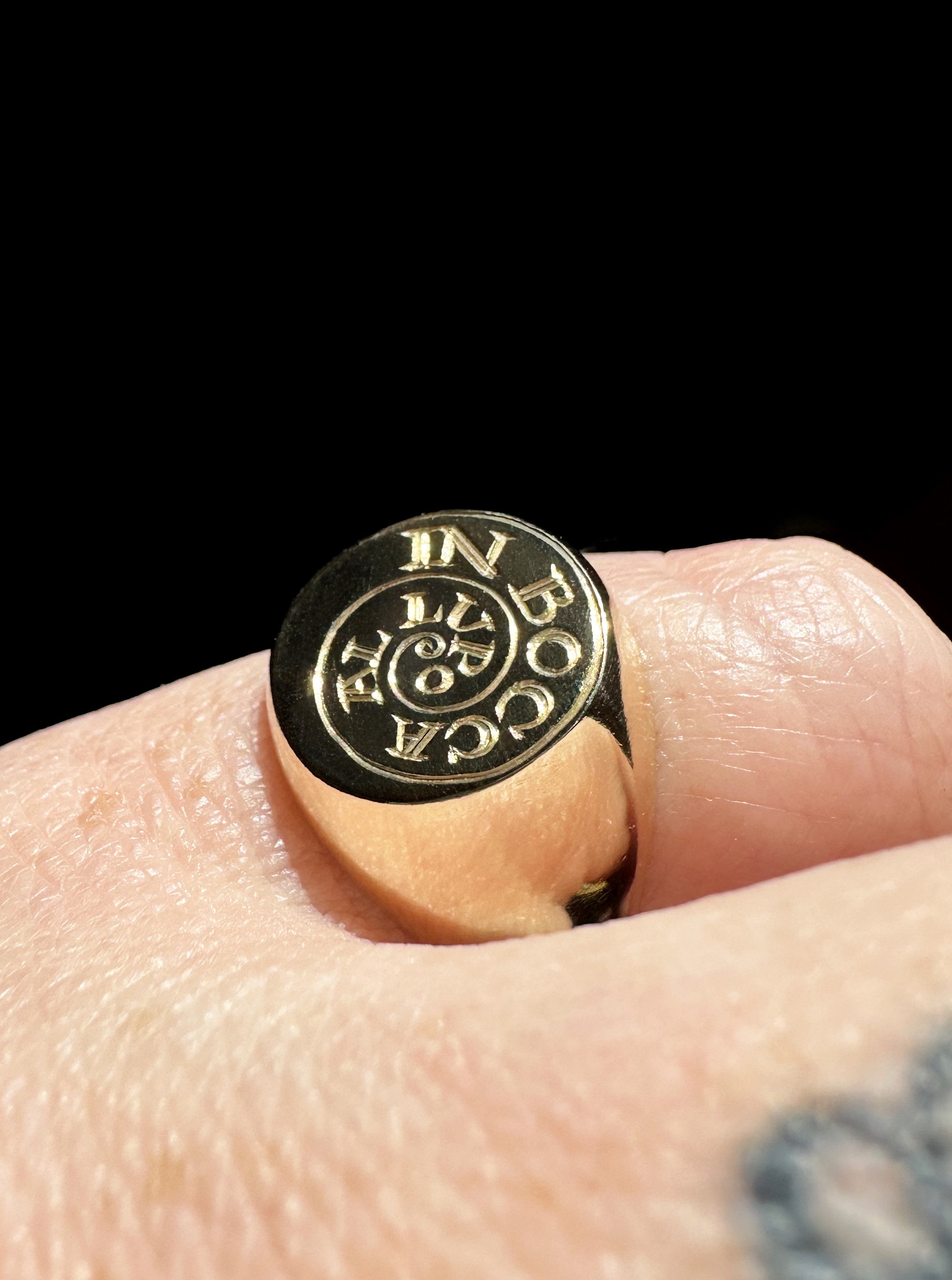 A yellow gold ring with hand engraved typography.