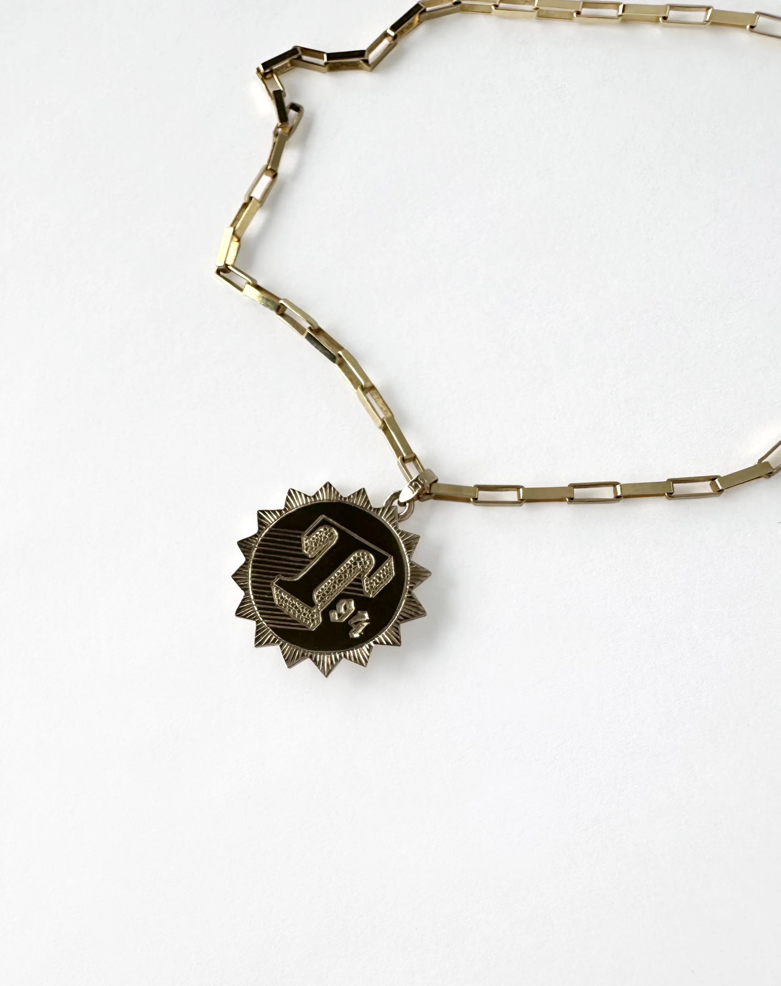 A silver chain necklace with a medal pendant featuring the number 1/4 and a sunburst design.