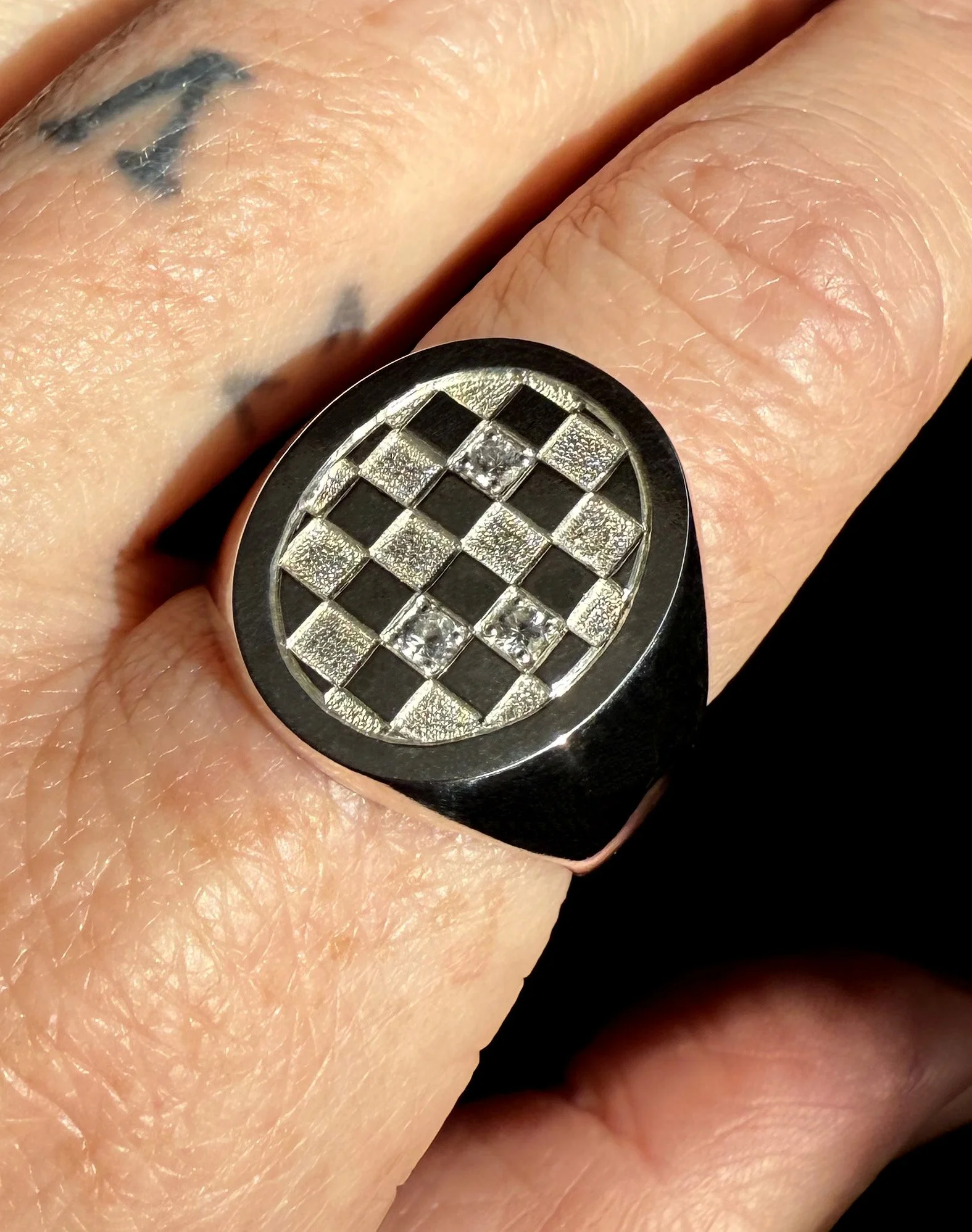 Oval gold ring with an engraved geometric checkered pattern and small embedded diamonds.