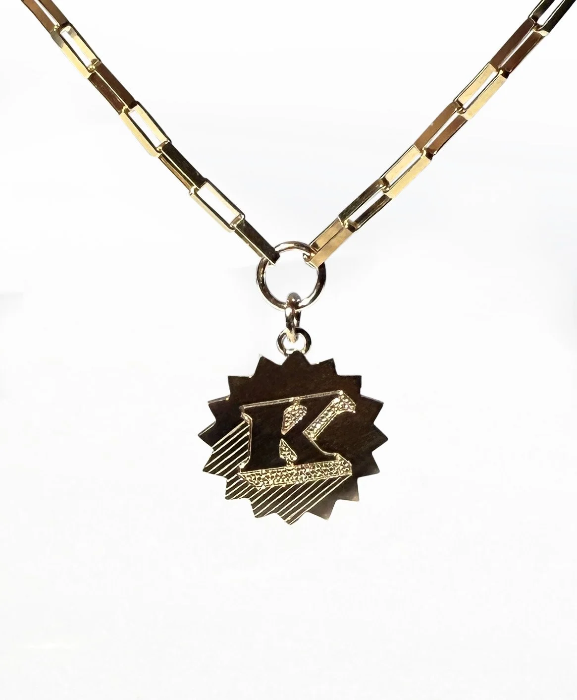 Close-up of a gold chain necklace with a circular pendant featuring a black background and a gold letter R.