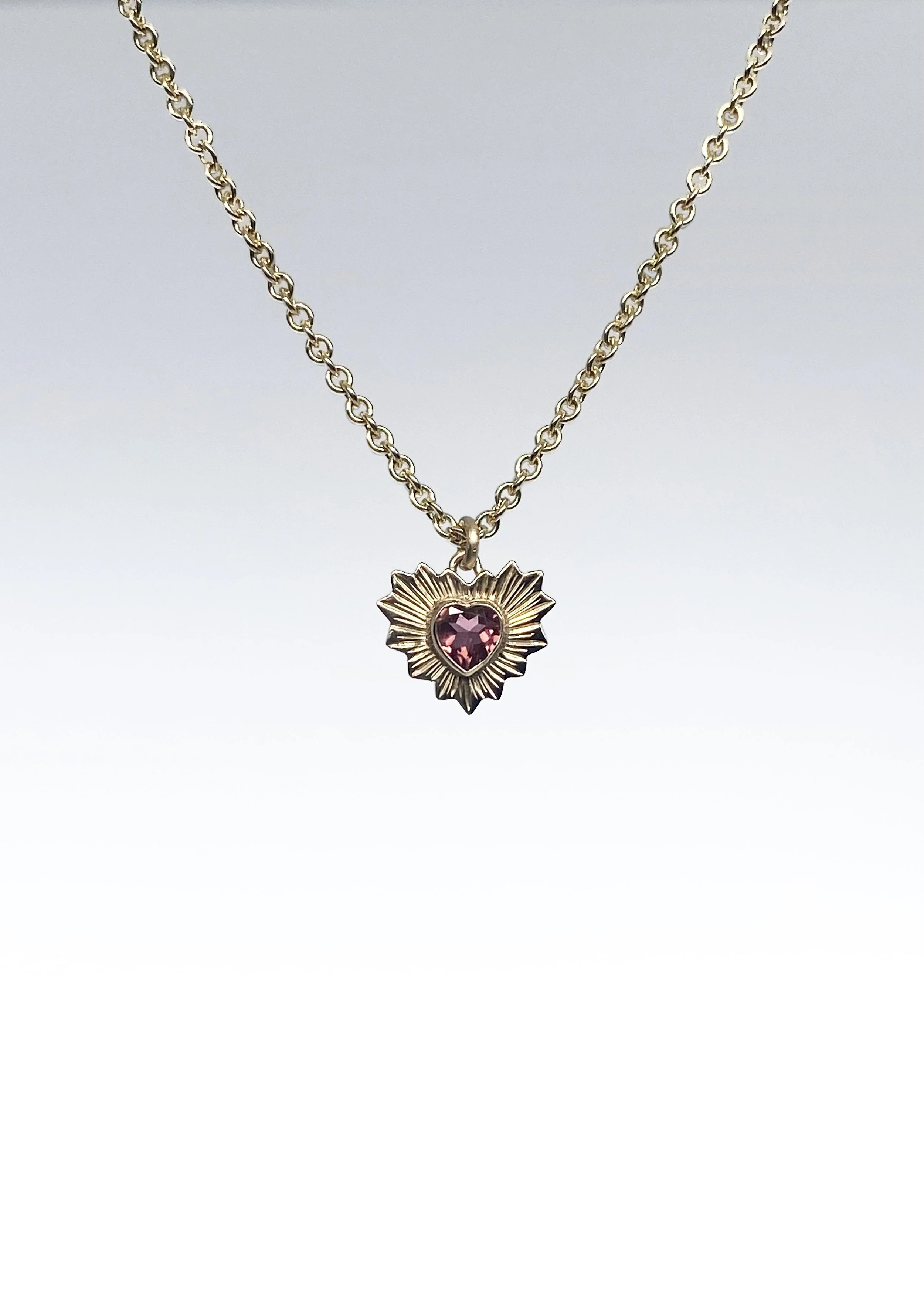 Gold necklace with a star-shaped pendant featuring a pink heart-shaped gemstone at the center.