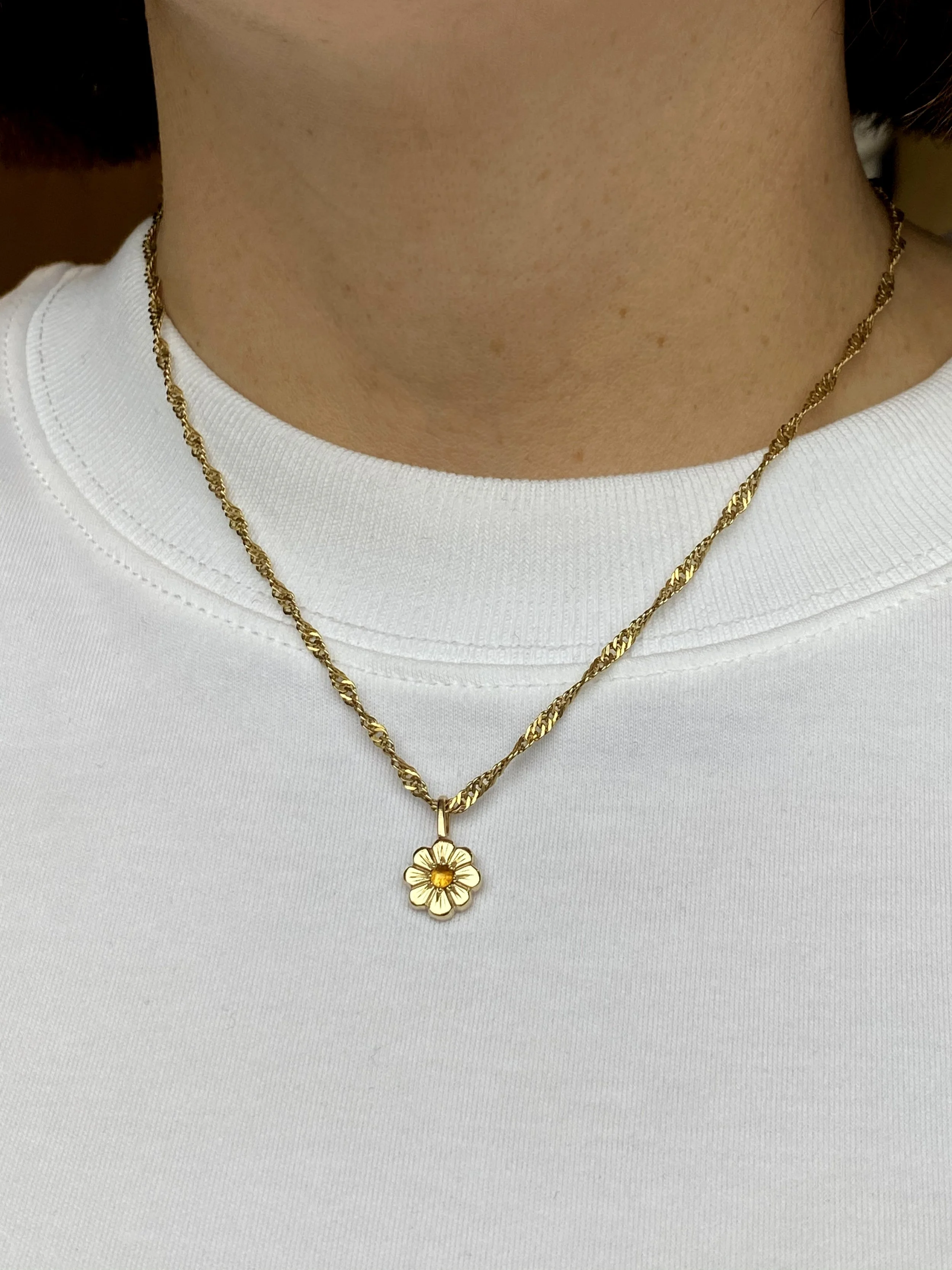Gold necklace with a flower-shaped pendant worn over a white shirt.