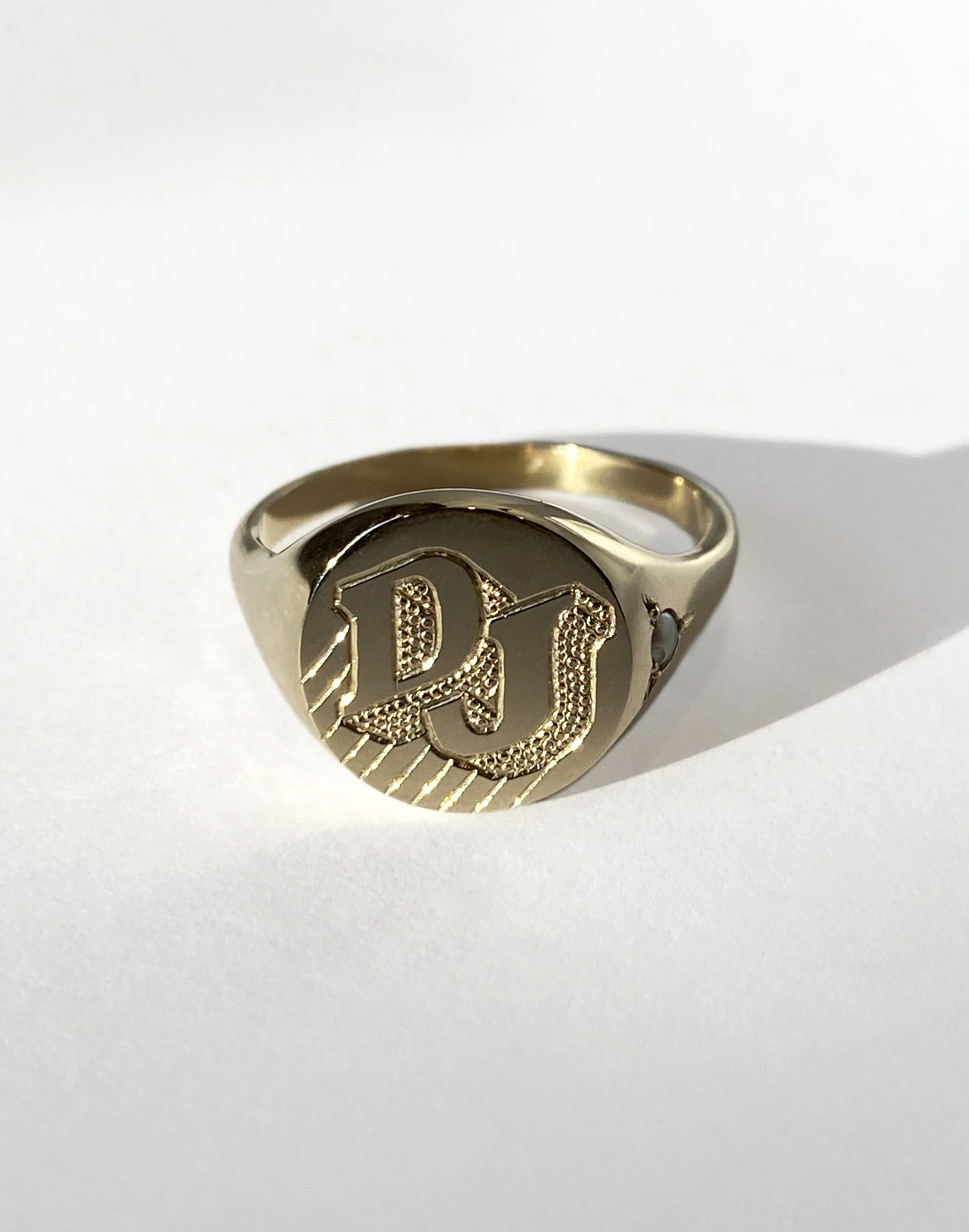Engraved gold signet ring featuring the capital letters 'D' and 'J'.
