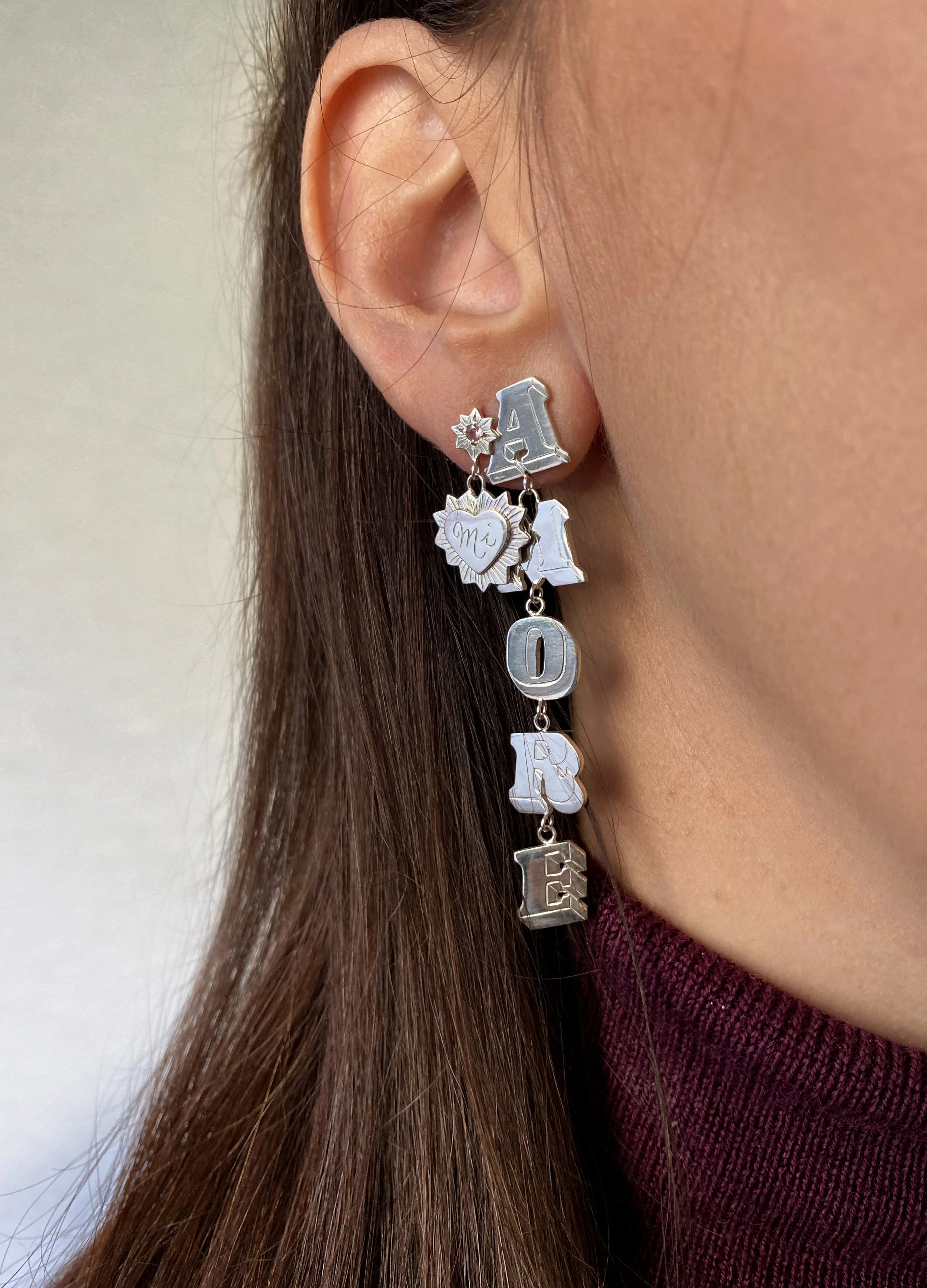 Amore earrings. The left earring has a 'Mi' engraved in a heart. The right earring spells 'Amore'. Each letter is hand engraved and connected with a link. 