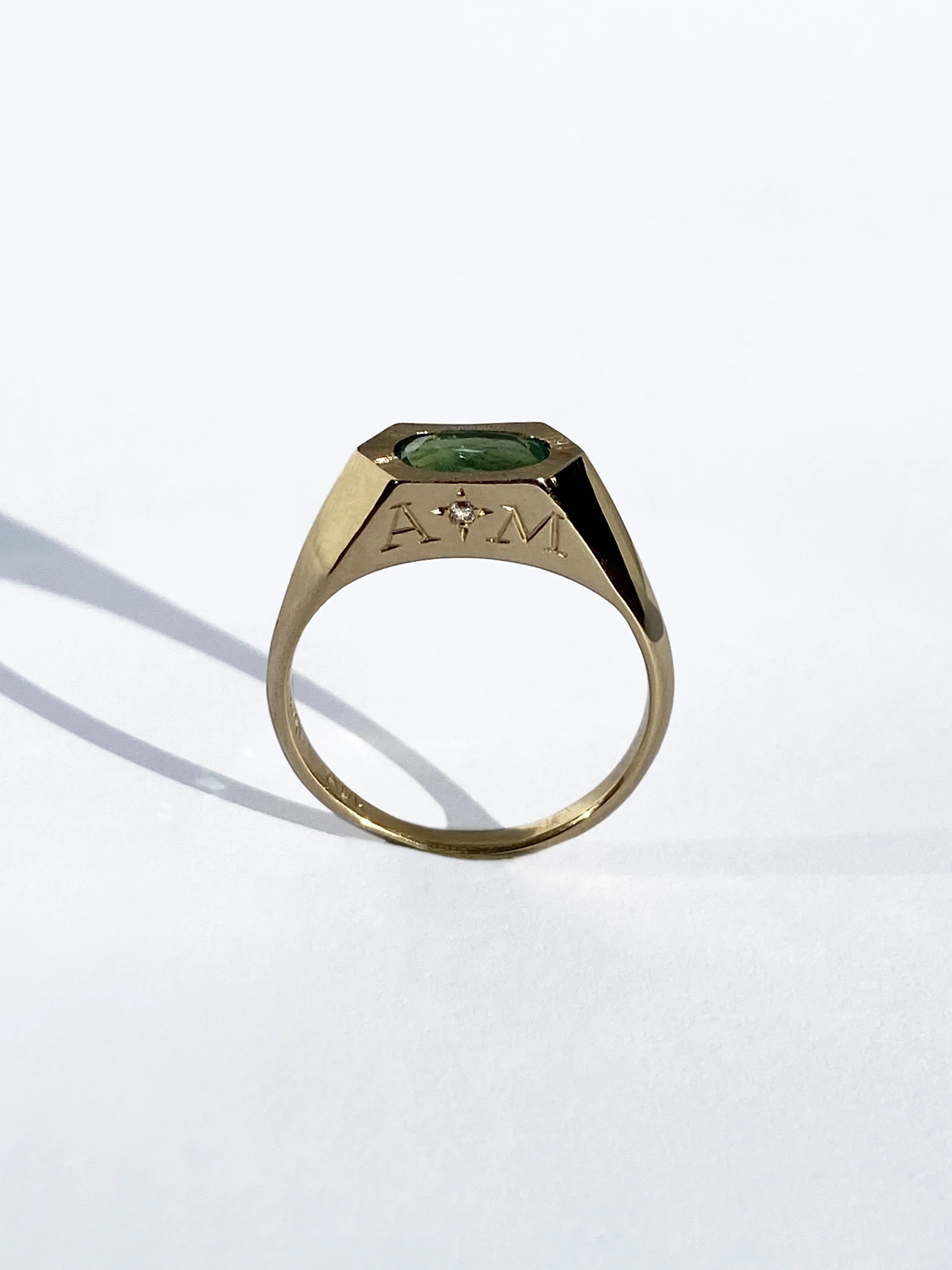 18ct gold ring with green gemstone and engraved letters A, M, and a small diamond.
