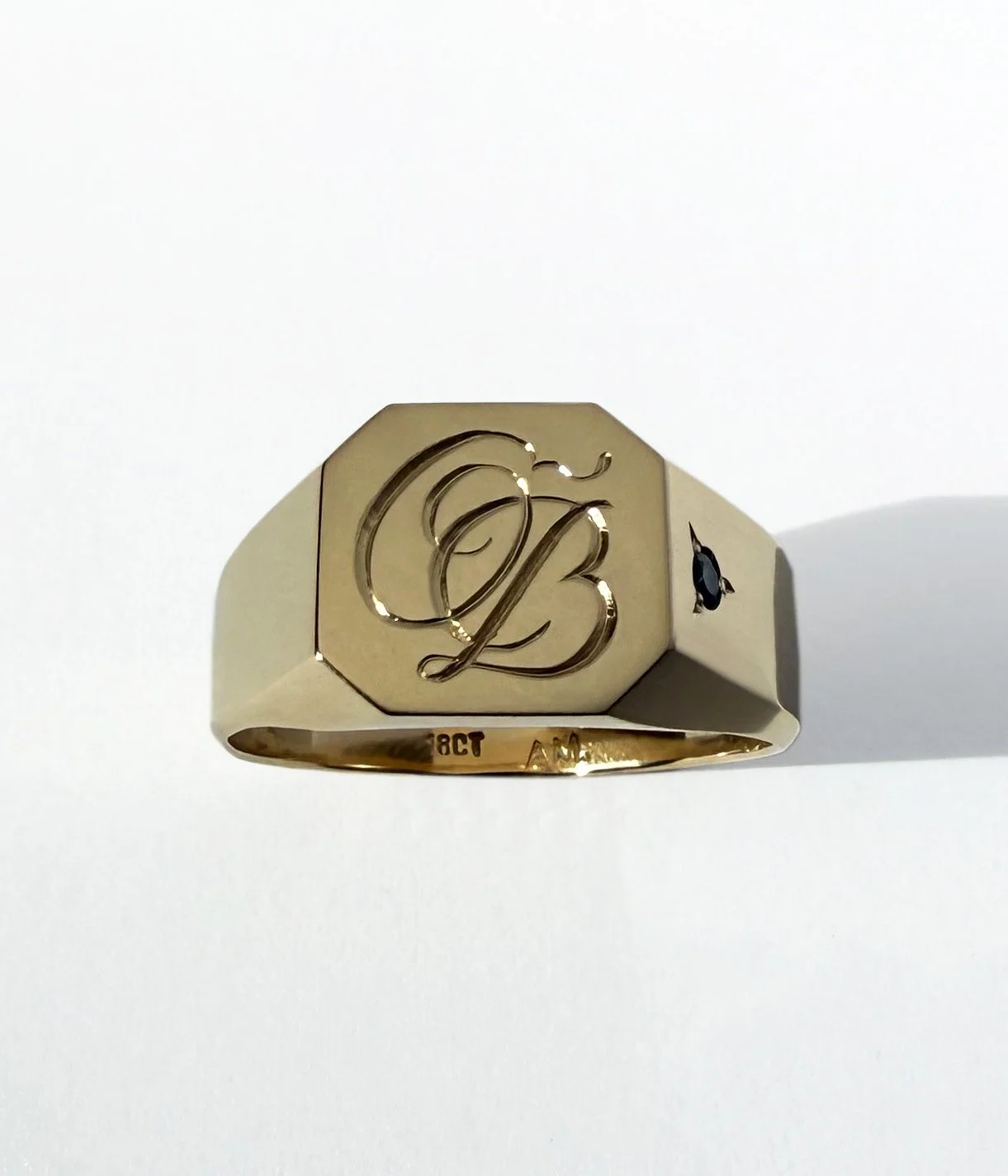 An 18 carat gold ring with a large engraved letter 'O' and 'B' on the top, featuring a sapphire on the side.