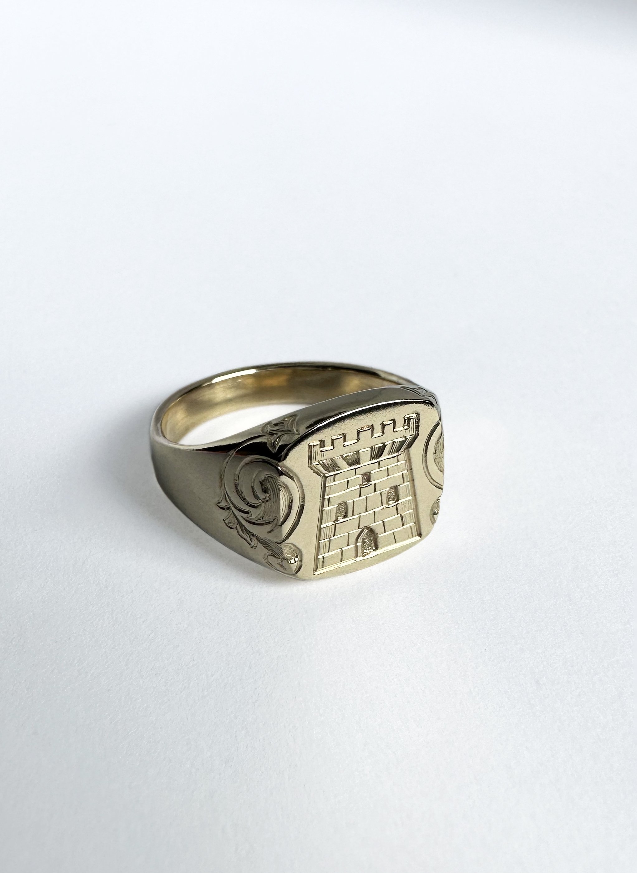 A gold ring with an engraving of a family crest of a castle.