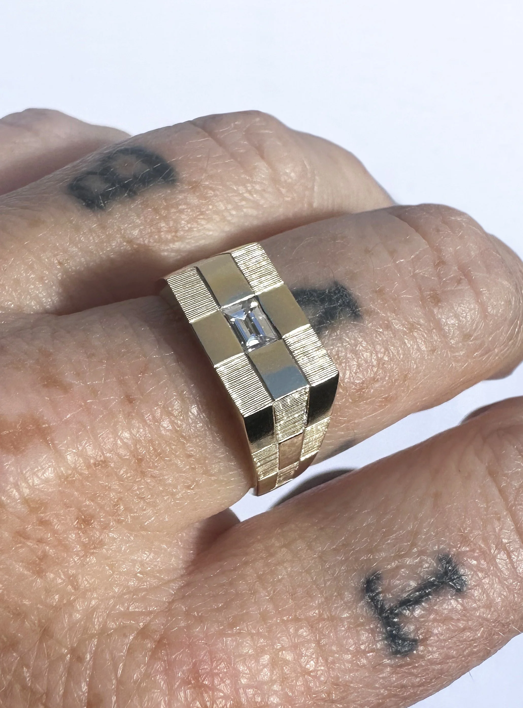 This hand engraved gold check ring set with a baguette diamond in the centre of the ring. 
