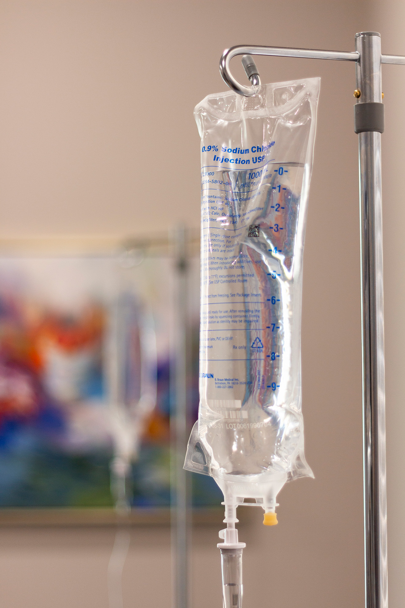 IV saline bag hanging from a stand, partially filled with clear liquid, in a medical setting.