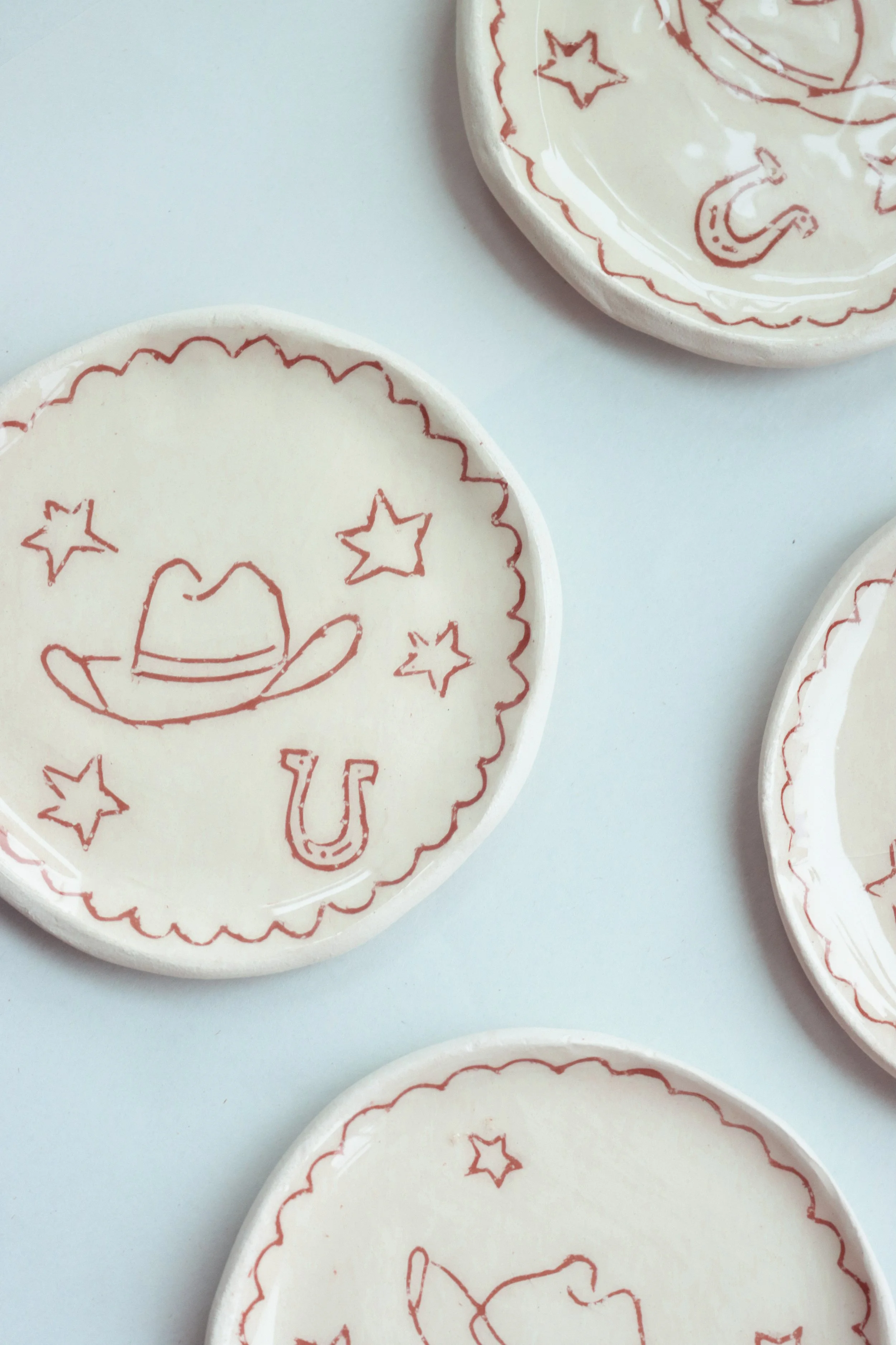 White ceramic coasters with a rust red illustration of a cowboy hat and stars on it.
