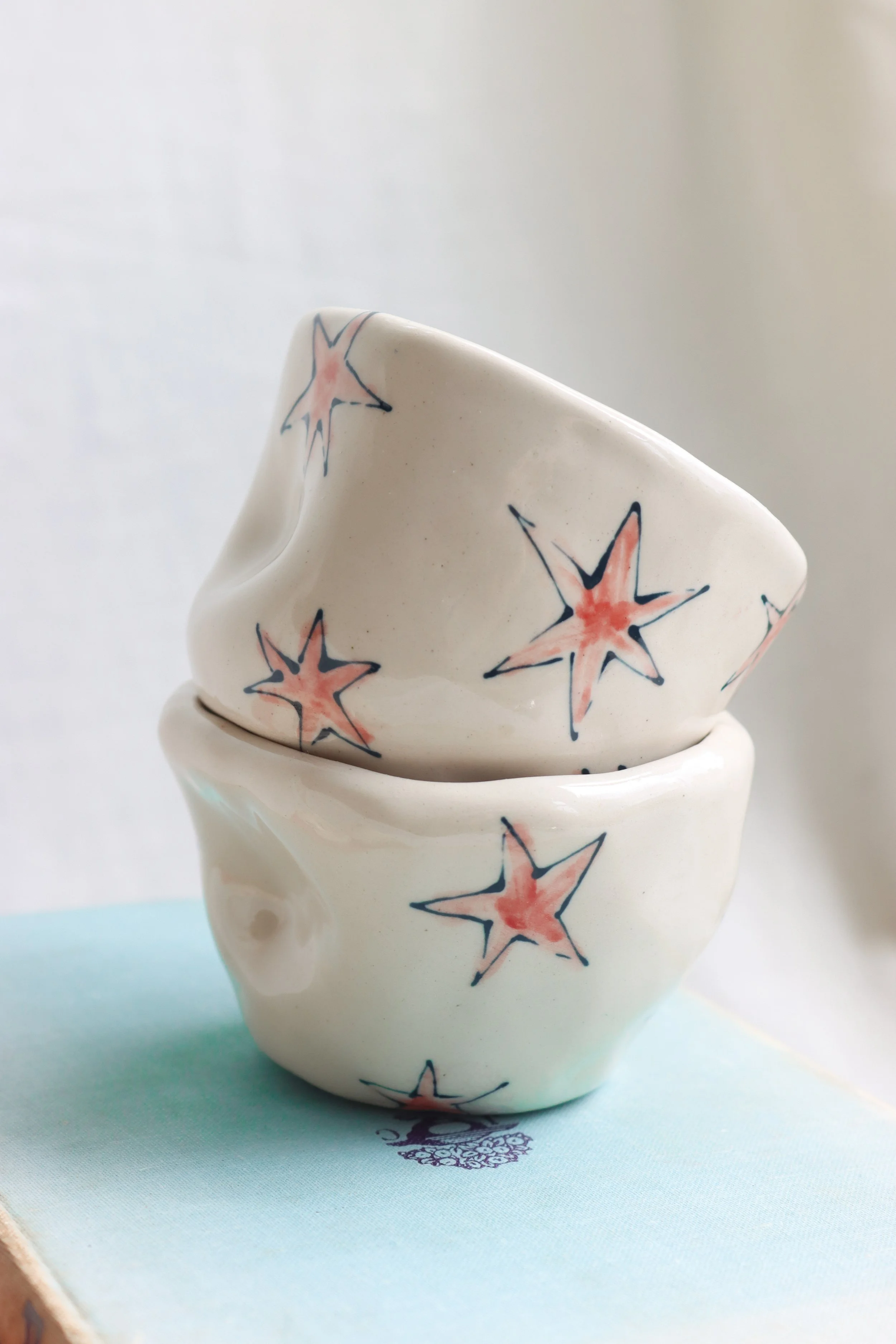 Two white ceramic cups stacked. Each one is covered with red stars with blue outlines.