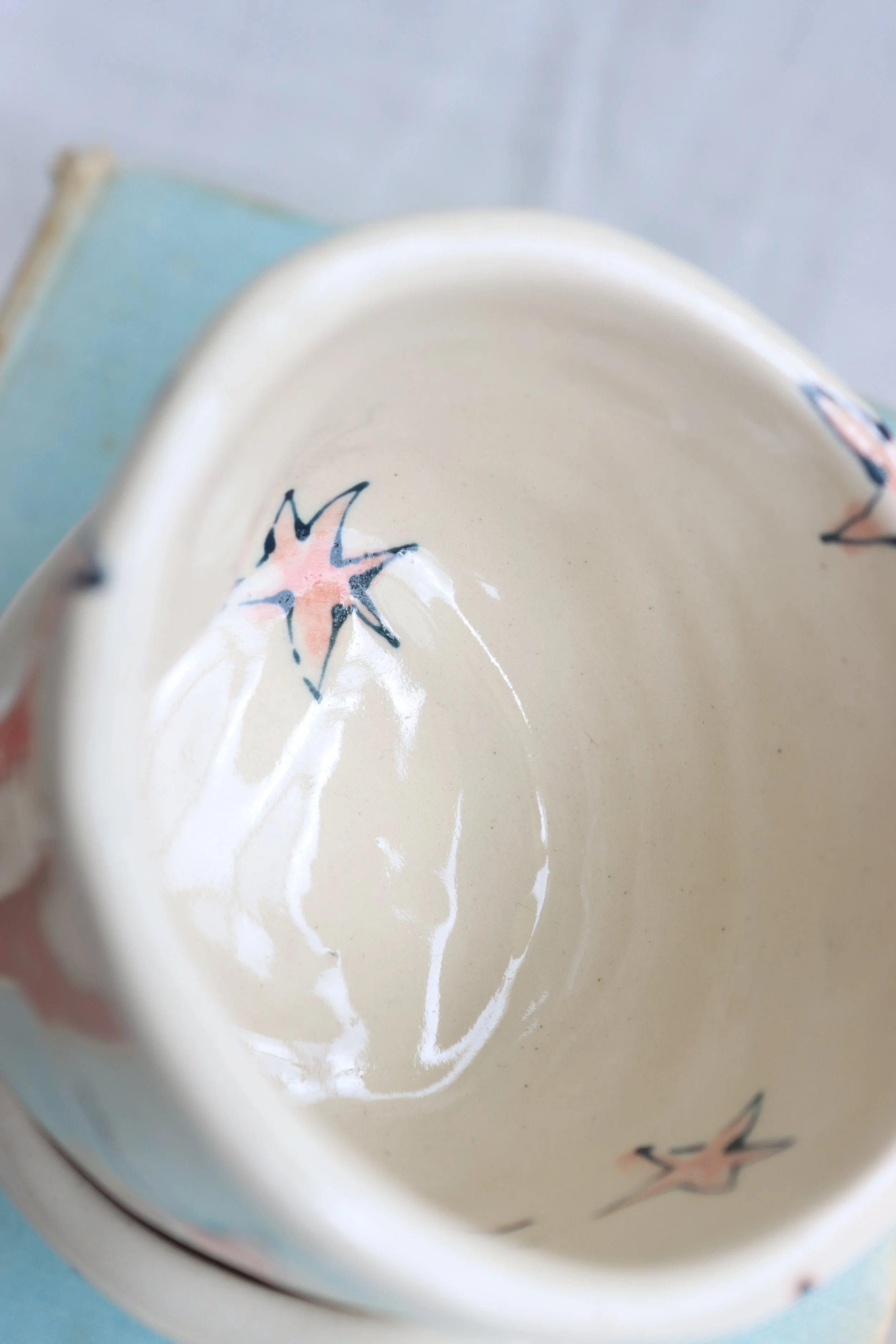 The inside of a cream ceramic cup, with red stars on it. The stars have blue outlines.